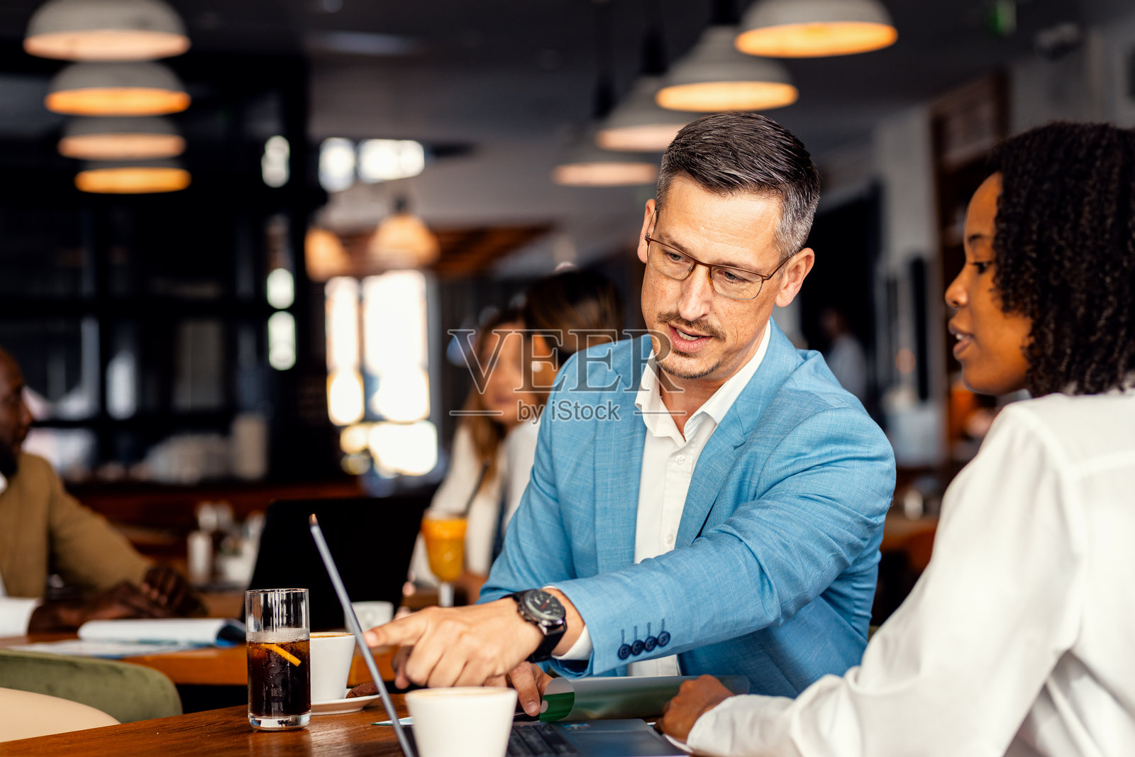 在现代咖啡馆，一位男商人和一位女同事正在使用笔记本电脑讨论工作。照片摄影图片