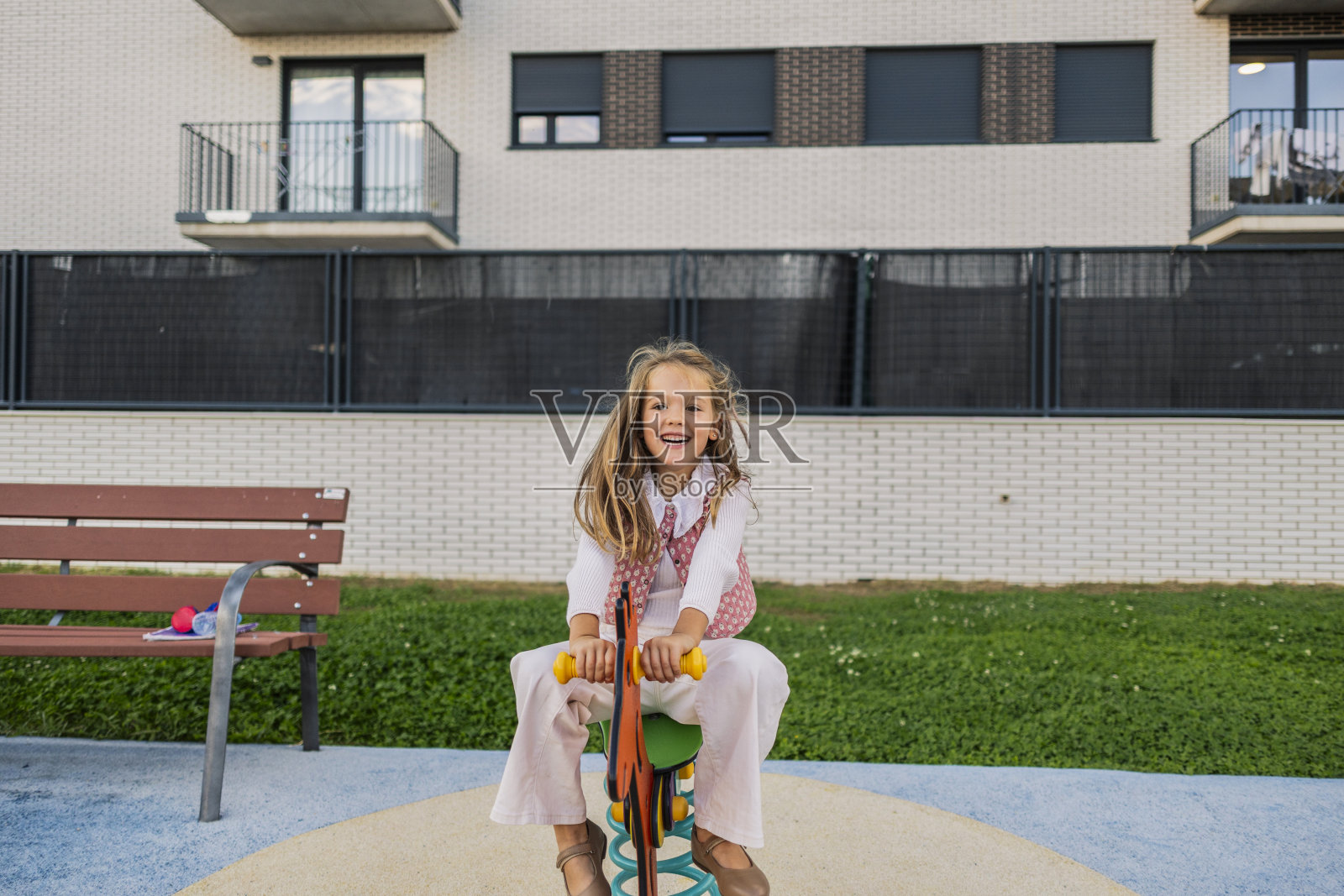 快乐的小女孩在游乐场的弹簧骑乘玩具上玩耍照片摄影图片