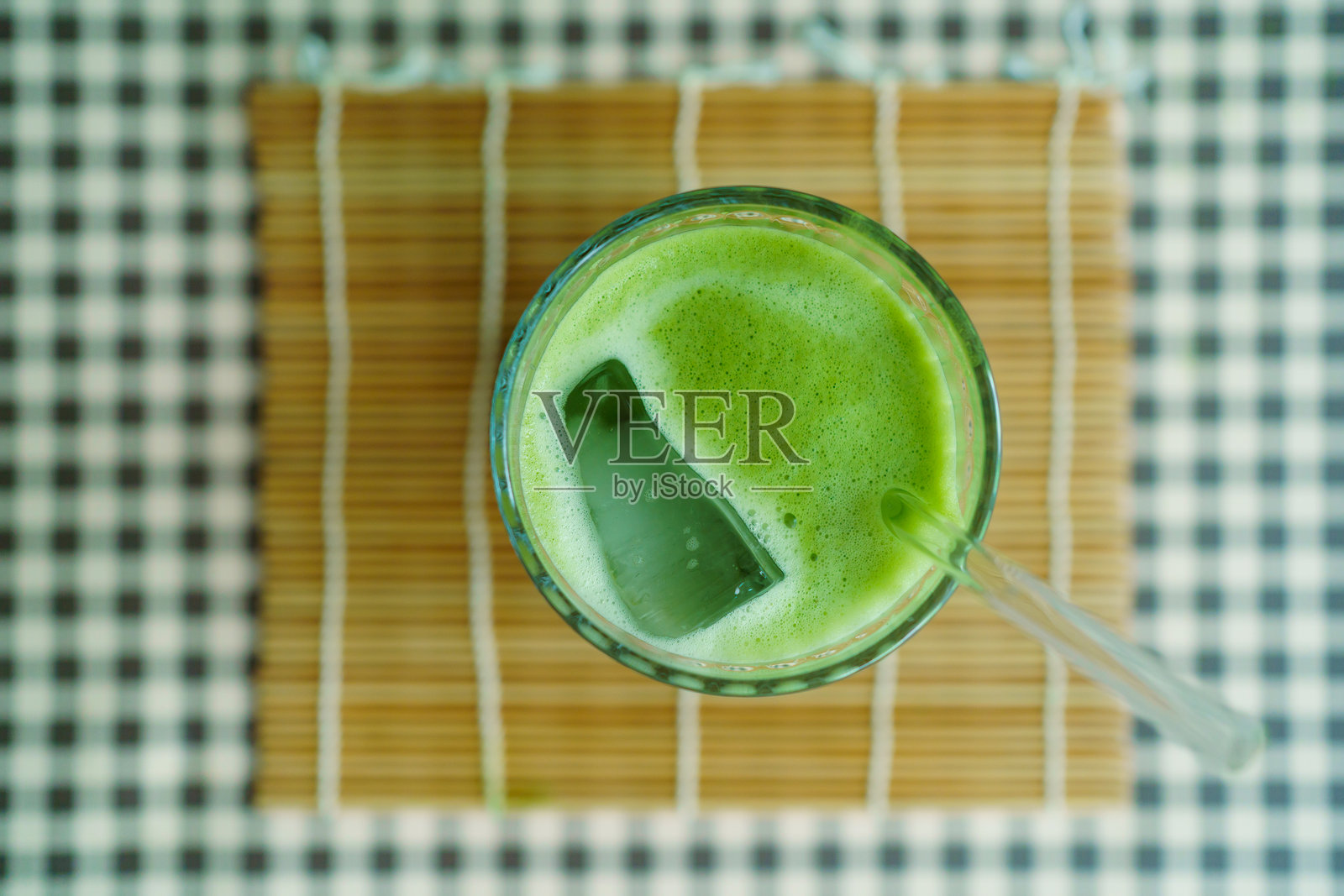 竹席上放着装有吸管的冰抹茶拿铁的玻璃杯，俯视拍摄。照片摄影图片
