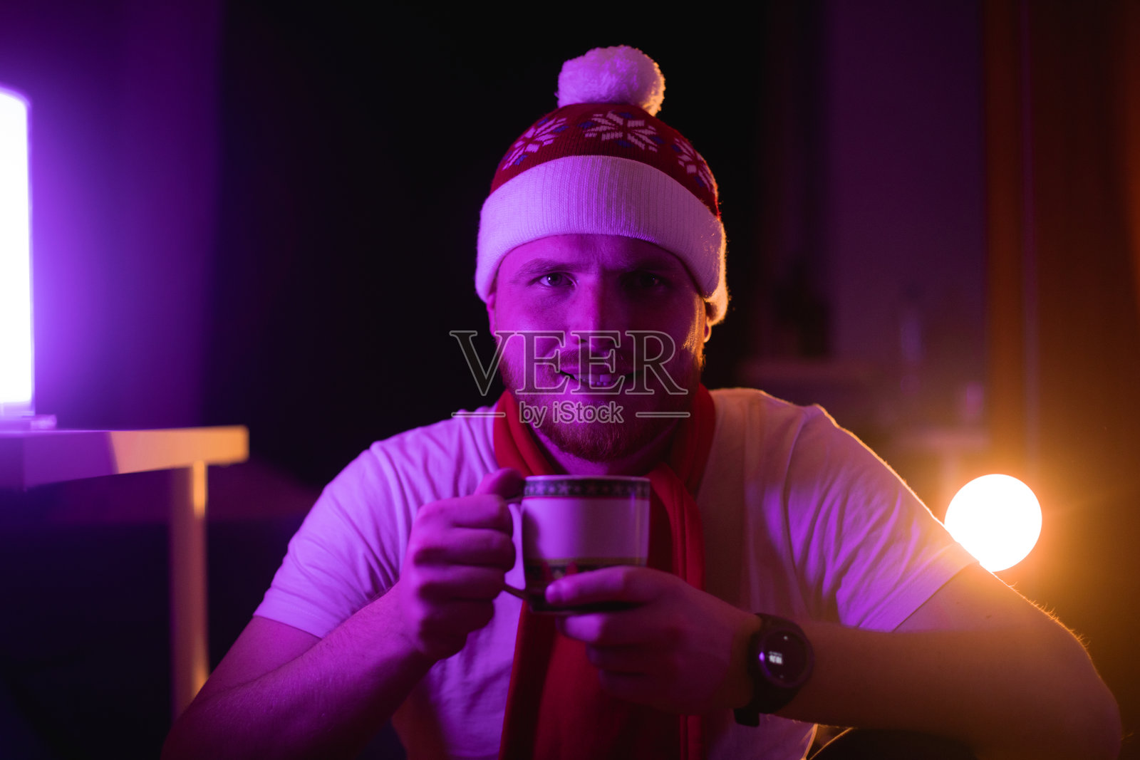 身处圣诞主题灯光下，男子手持节日马克杯静坐照片摄影图片