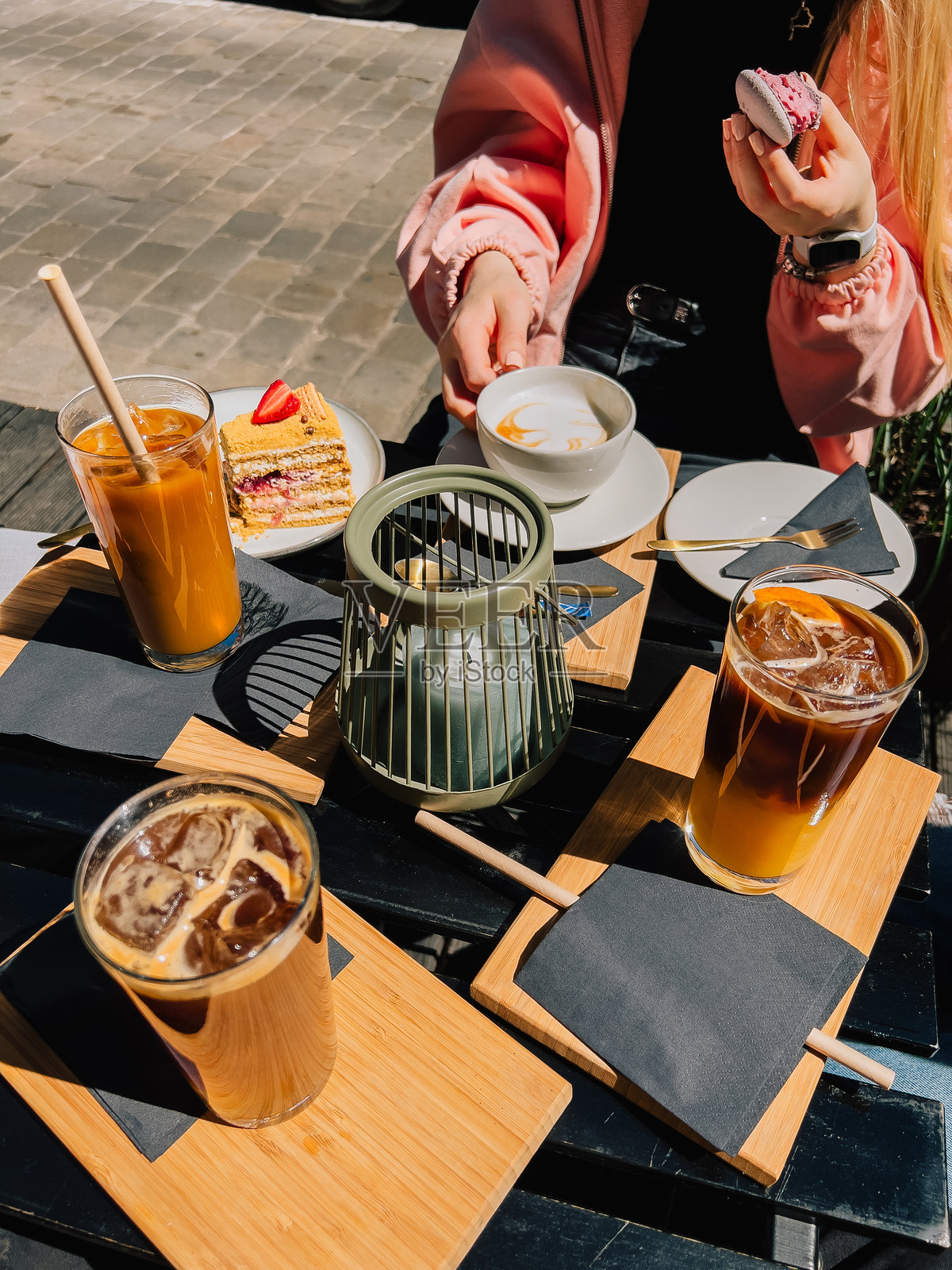 女子在阳光明媚的日子里，于户外咖啡馆享受清爽的休憩时光，品尝冰咖啡、一层层叠加上草莓的蛋糕，以及色彩缤纷的马卡龙。朋友们也在户外咖啡馆放松，一同分享。照片摄影图片