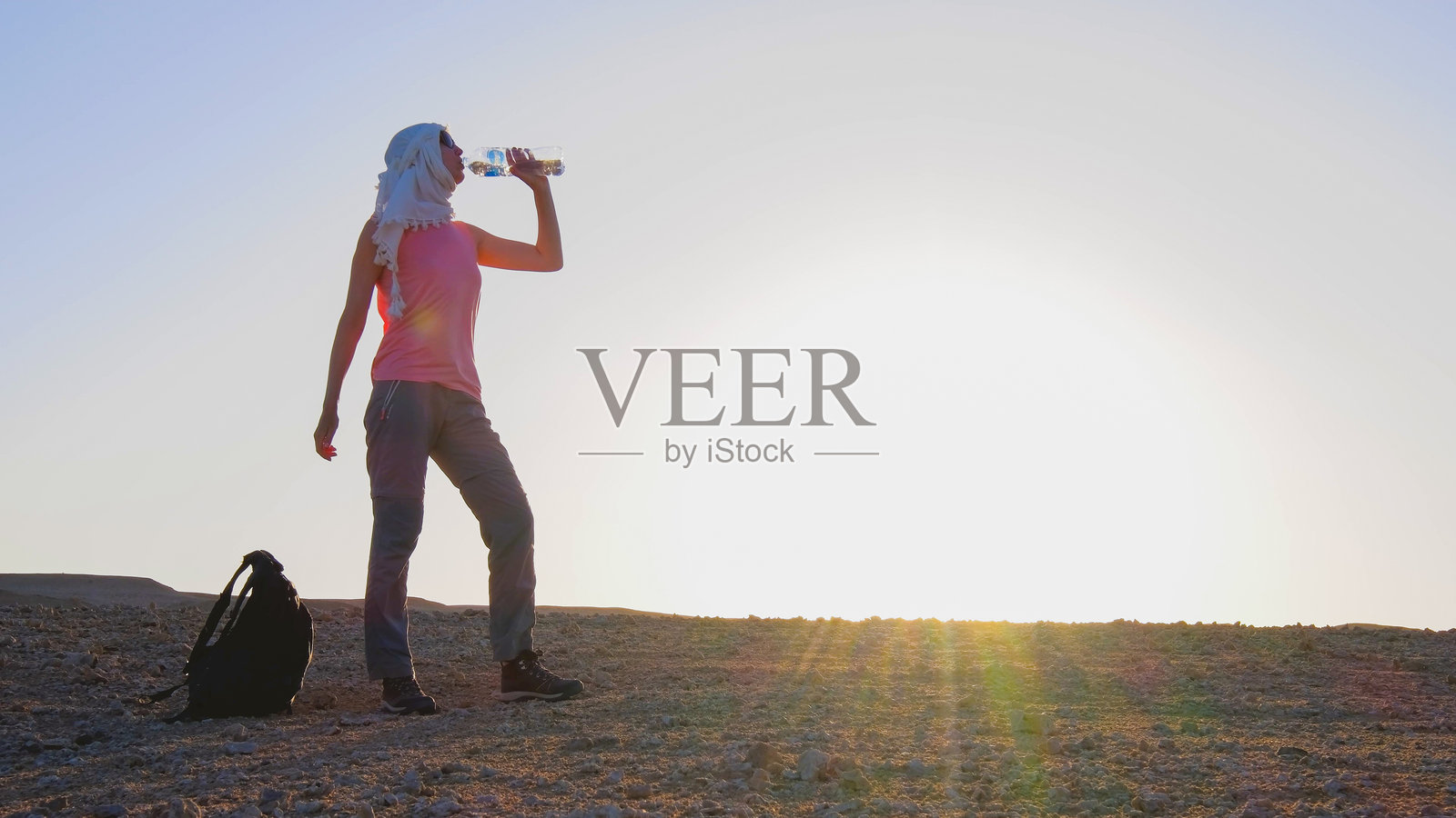 一名旅行者在埃及沙漠日落时喝水。照片摄影图片