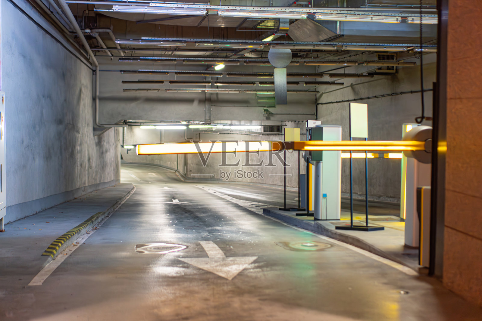 地下停车场，混凝土天花板，露出的管道和风道，嵌入式人造灯光投下阴影，标志指示车辆移动方向照片摄影图片