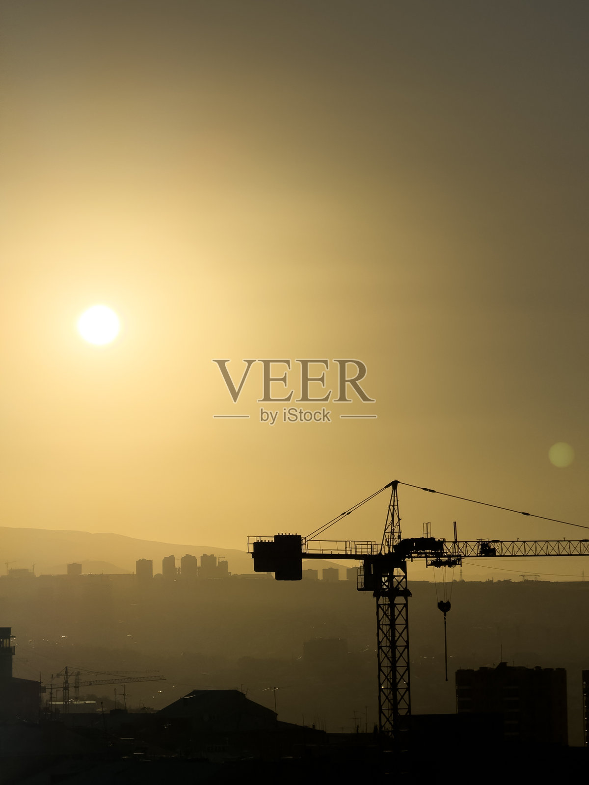 白天，明媚的阳光下，城市背景中矗立着一座建筑起重机。起重机在城市上方的天空中。照片摄影图片