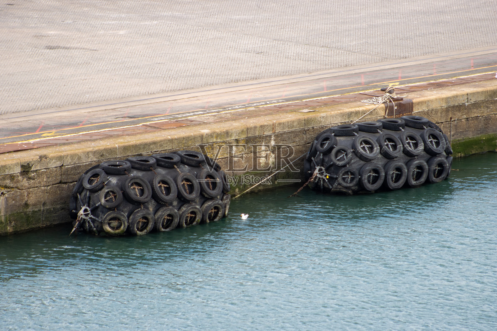 巨大的黑色挡泥板绑在由塑料和汽车轮胎制成的水泥码头上，旁边是淡蓝色的水照片摄影图片