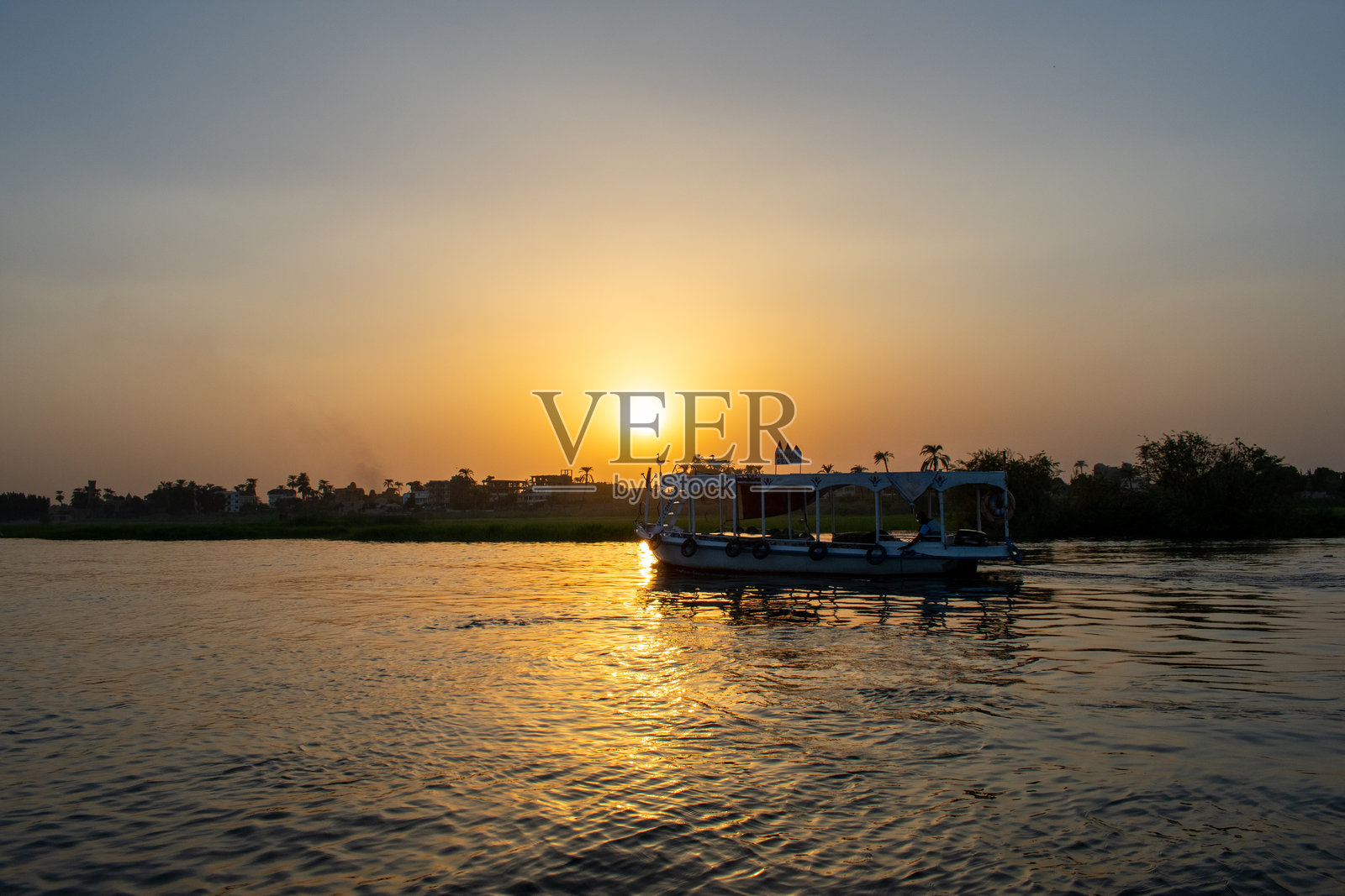 埃及卢克索，尼罗河上的船只与日落天空，水边有建筑和城市。照片摄影图片