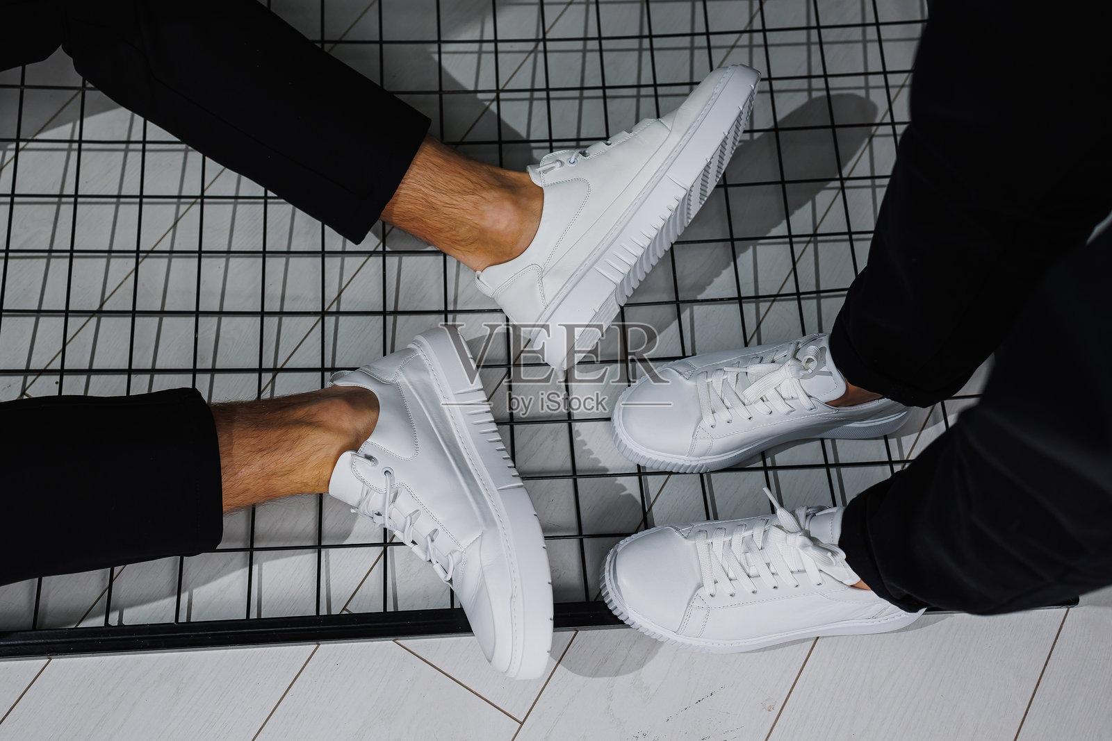 夏日鞋履。男性和女性腿部特写，身着黑色裤子和白色休闲运动鞋。男女皆宜的夏季皮鞋。照片摄影图片