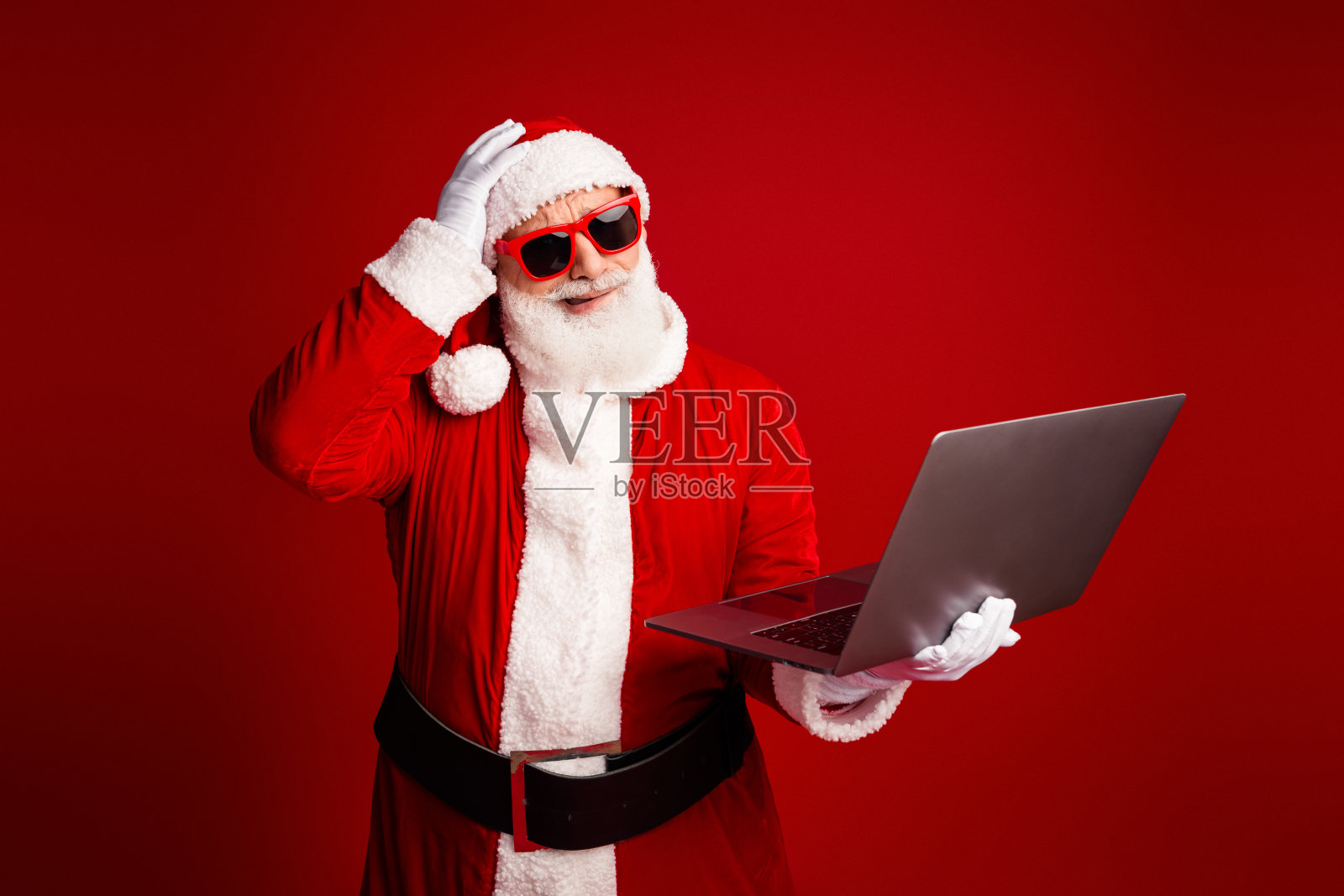 圣诞老人身穿红色服装，手持笔记本电脑，在节日气氛浓厚的影棚中，准备进行假日营销和圣诞季推广。照片摄影图片