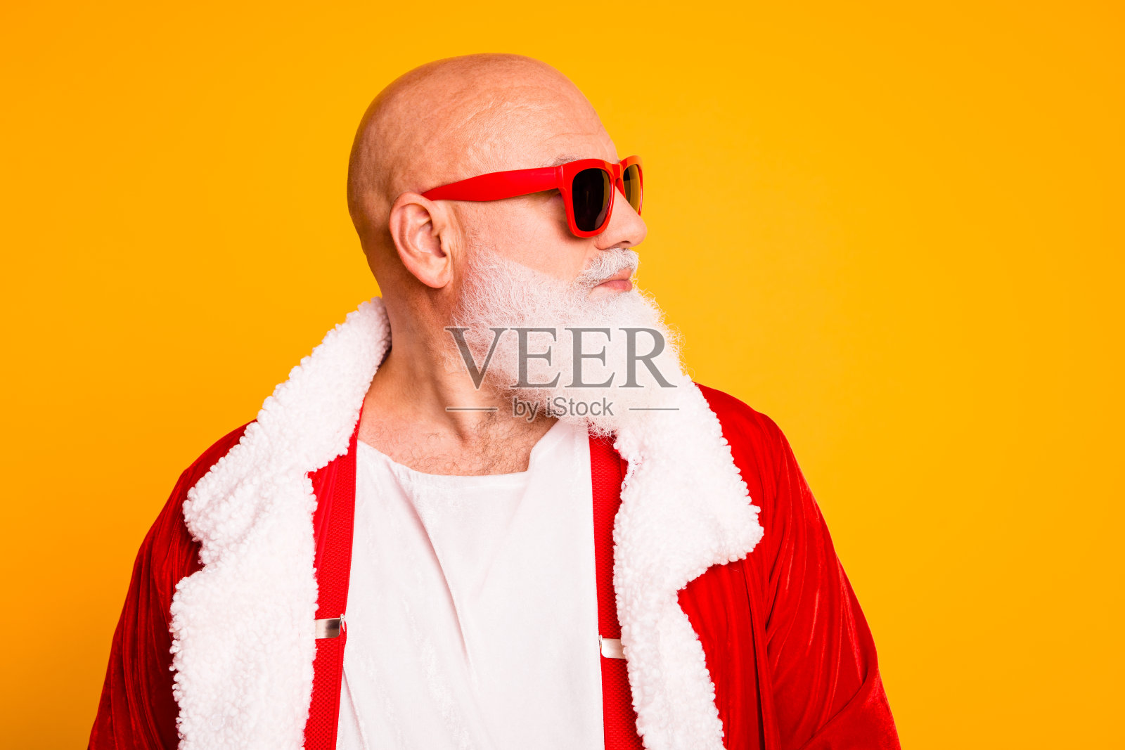 圣诞老人造型的爷爷，身着带白色毛边的红色服装，戴着红色太阳镜，背景为明亮的黄色照片摄影图片