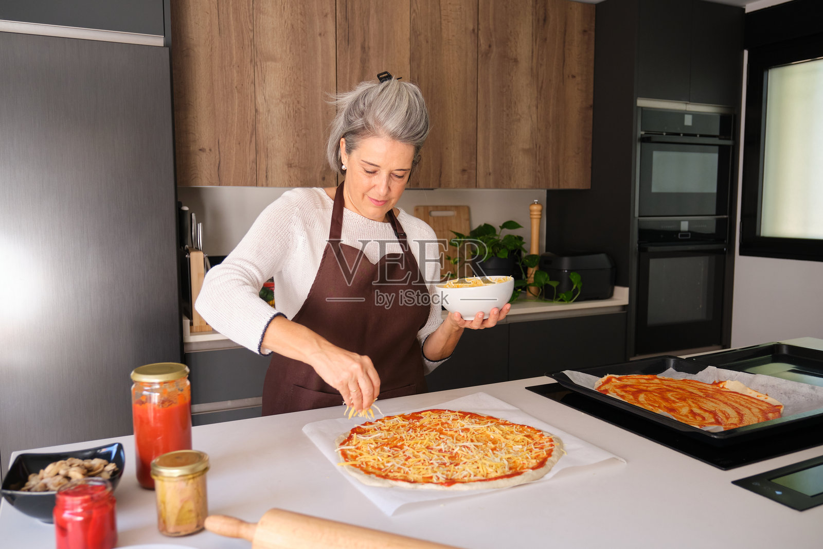 老年女性在家制作披萨，上面撒着奶酪照片摄影图片