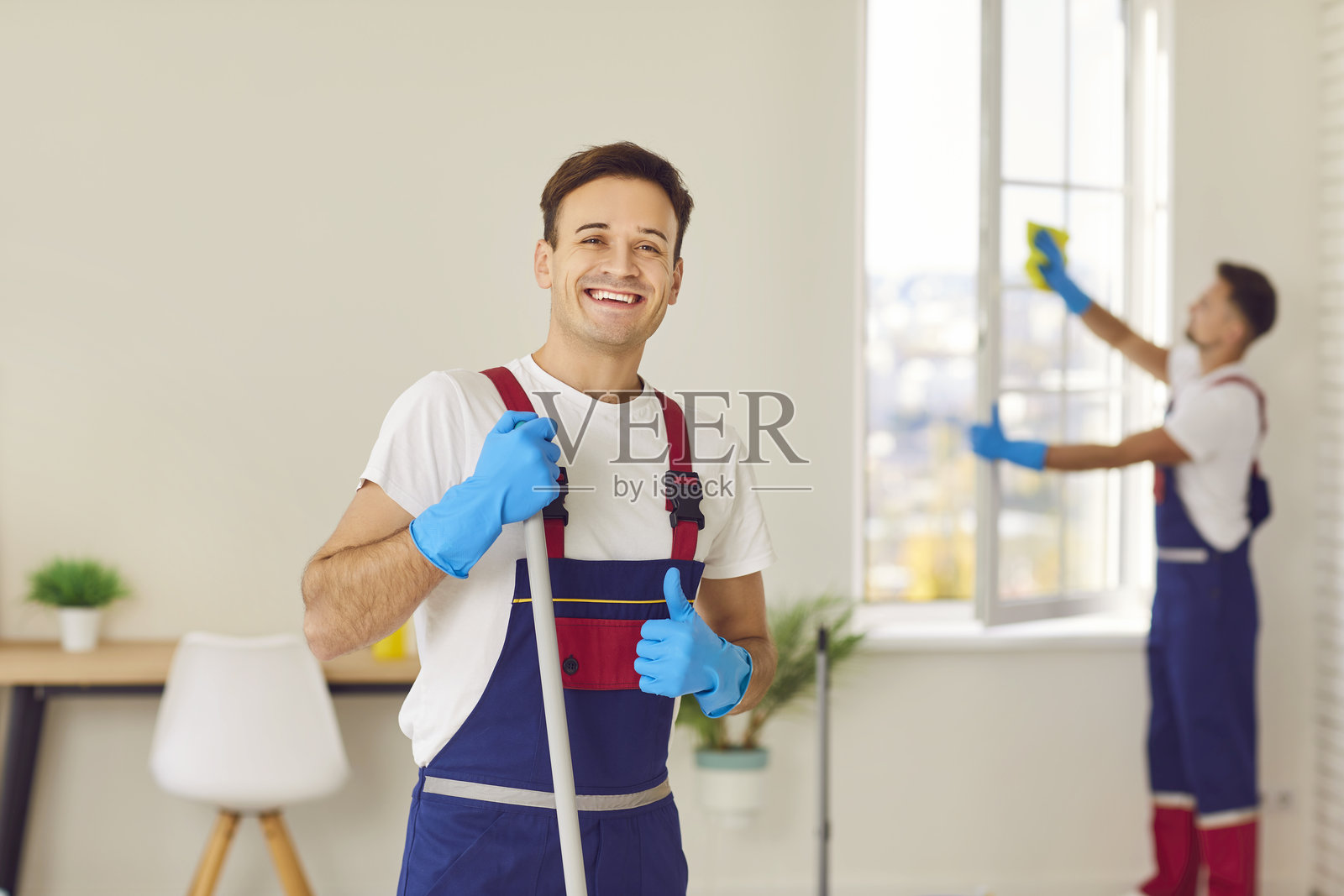 穿着专业清洁服务制服的快乐清洁工看向镜头。照片摄影图片