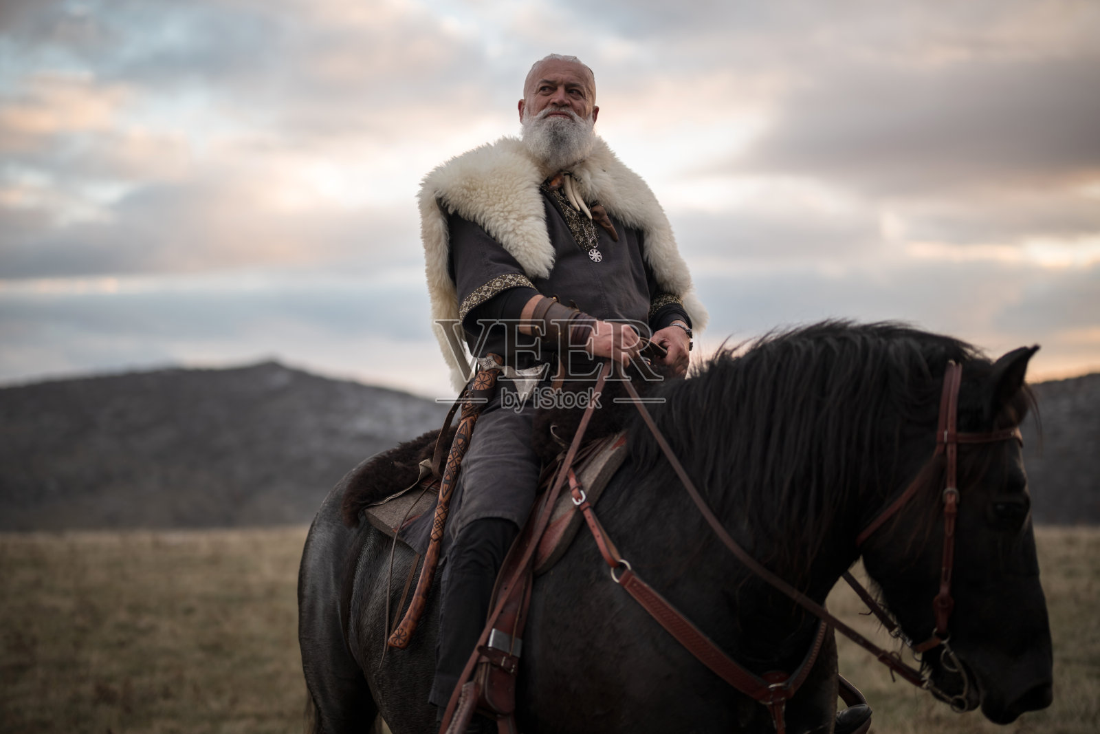 身披毛皮斗篷的维京战士骑着一匹巨大的黑马，在日落时分审视着壮丽的风景。这幅画面唤起了对古代探索、冒险和狂野精神的遐想。照片摄影图片