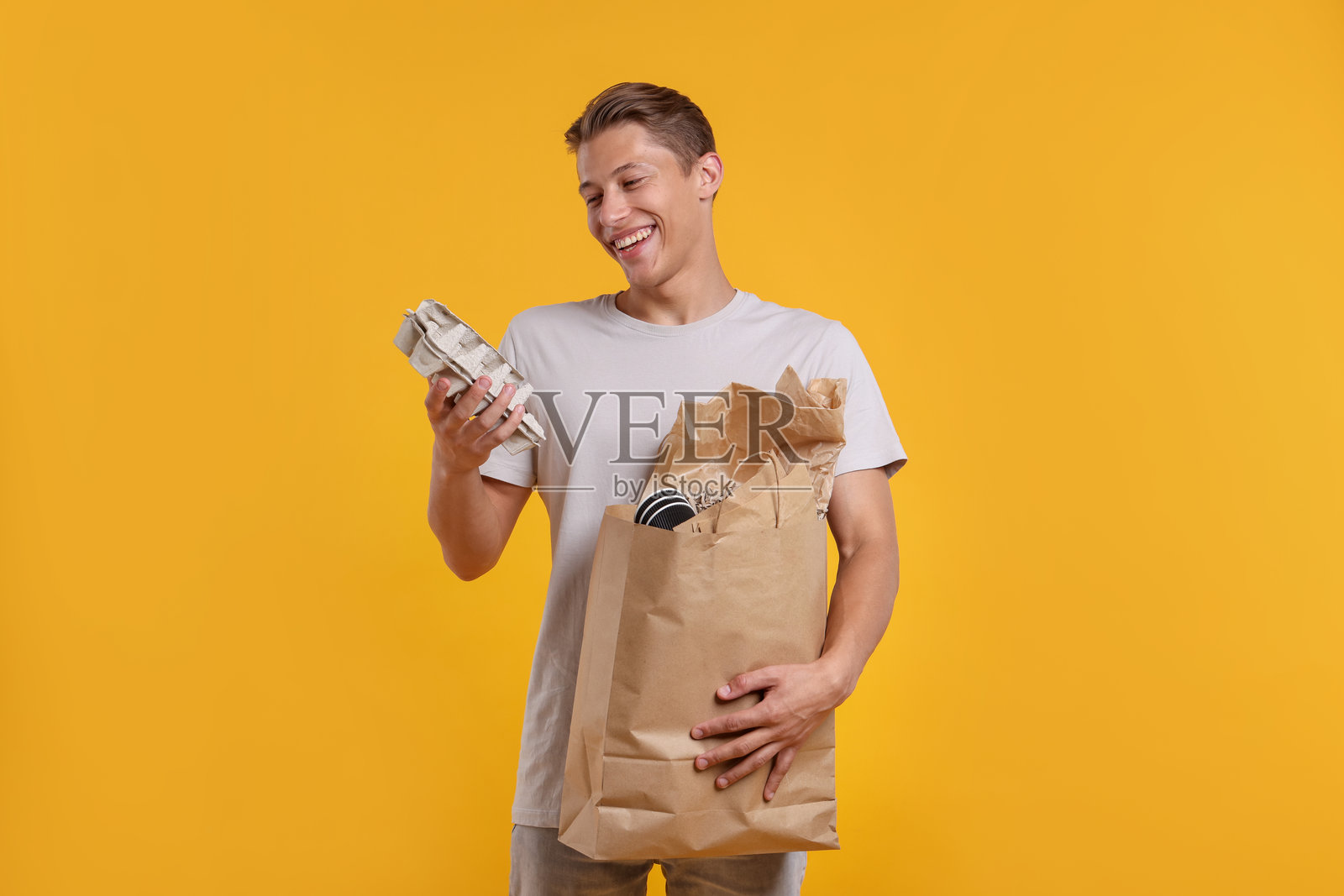 回收。一位面带微笑的男士，手提一袋装满各类废纸的袋子，背景为黄色照片摄影图片