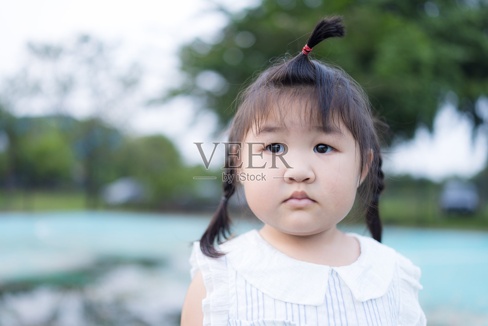 一个可爱的小亚裔女孩站在户外游乐场，她微笑着，张开双臂。公园里有各种游乐设施，包括秋千和长椅。照片摄影图片