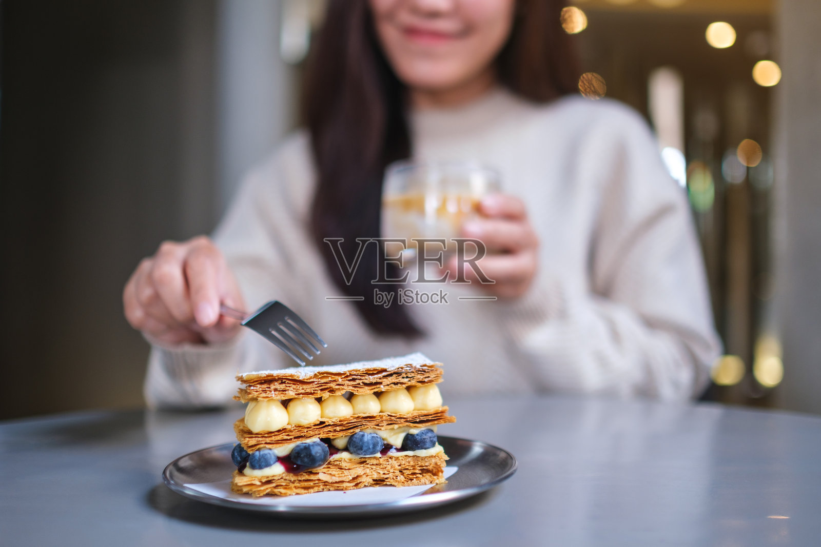 咖啡馆里，女子特写镜头，她正享用一块蓝莓千层酥，并喝着咖啡。照片摄影图片