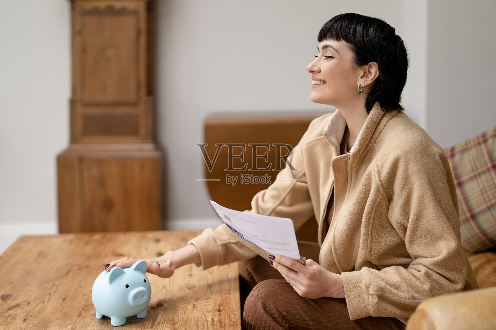 女子在家中一边查看财务文件，一边用存钱罐储蓄照片摄影图片