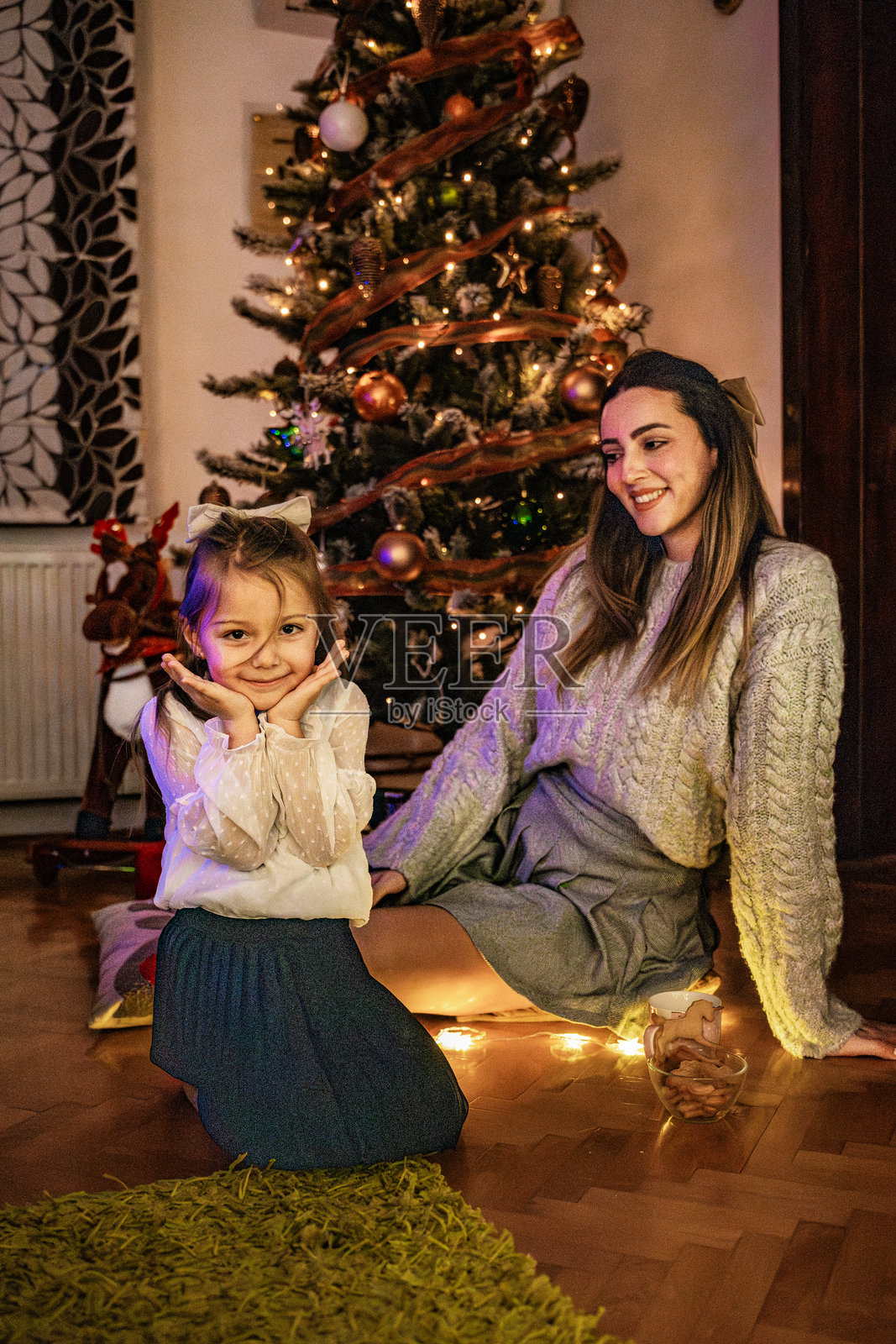 圣诞晚间，母女俩在圣诞树前分享温馨的爱意瞬间。包含节礼日、假期季以及新年庆祝活动。照片摄影图片