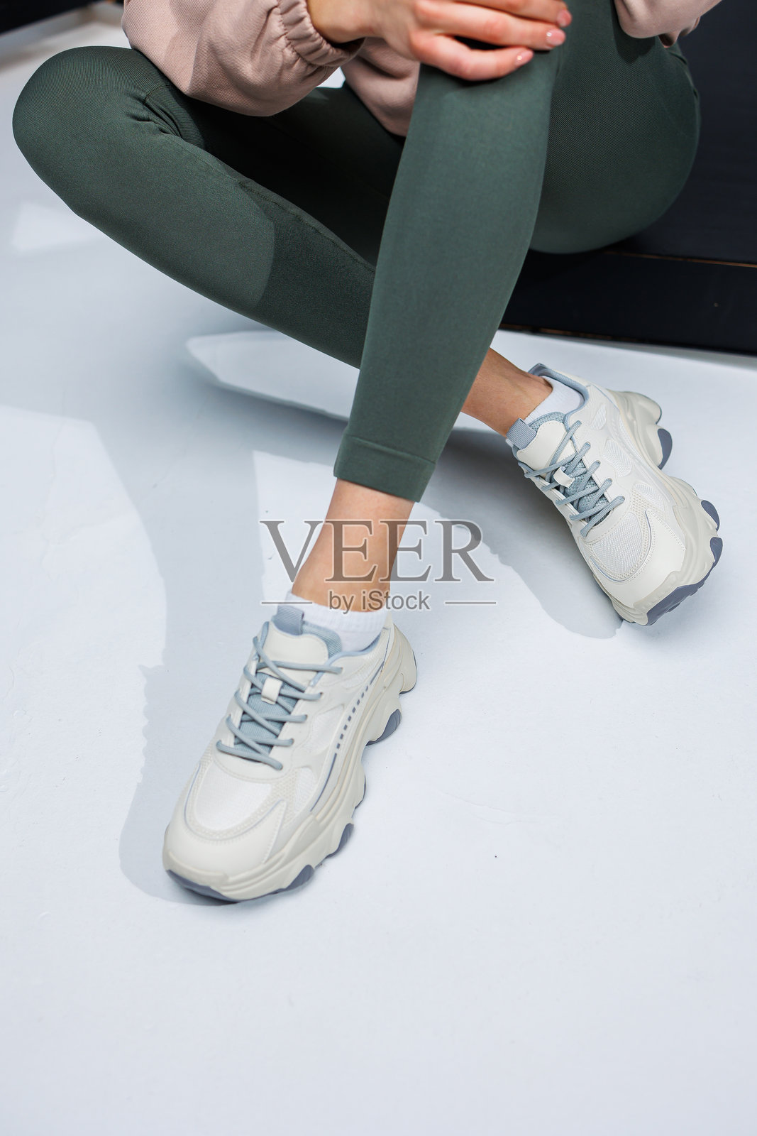 穿着紧身裤和白色时尚休闲运动鞋的苗条女性腿部。舒适的女士夏季鞋款。照片摄影图片