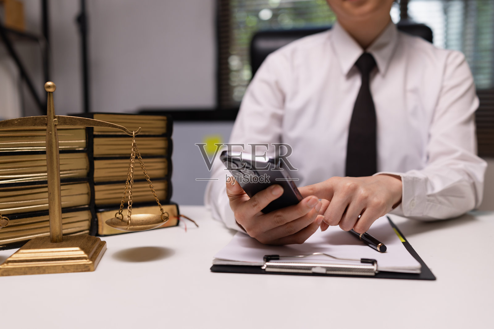 身着职业套装的律师正在现代办公室使用手机，背景有法律书籍。照片摄影图片