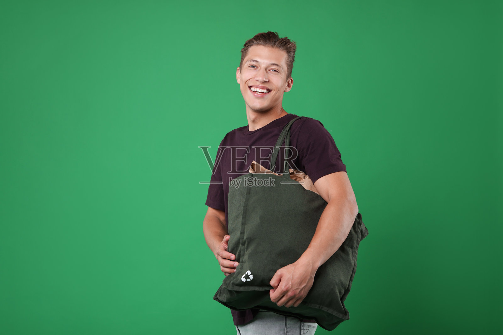 回收。一个微笑着的男人，手里拿着装满各种废纸的袋子，背景是绿色的。照片摄影图片