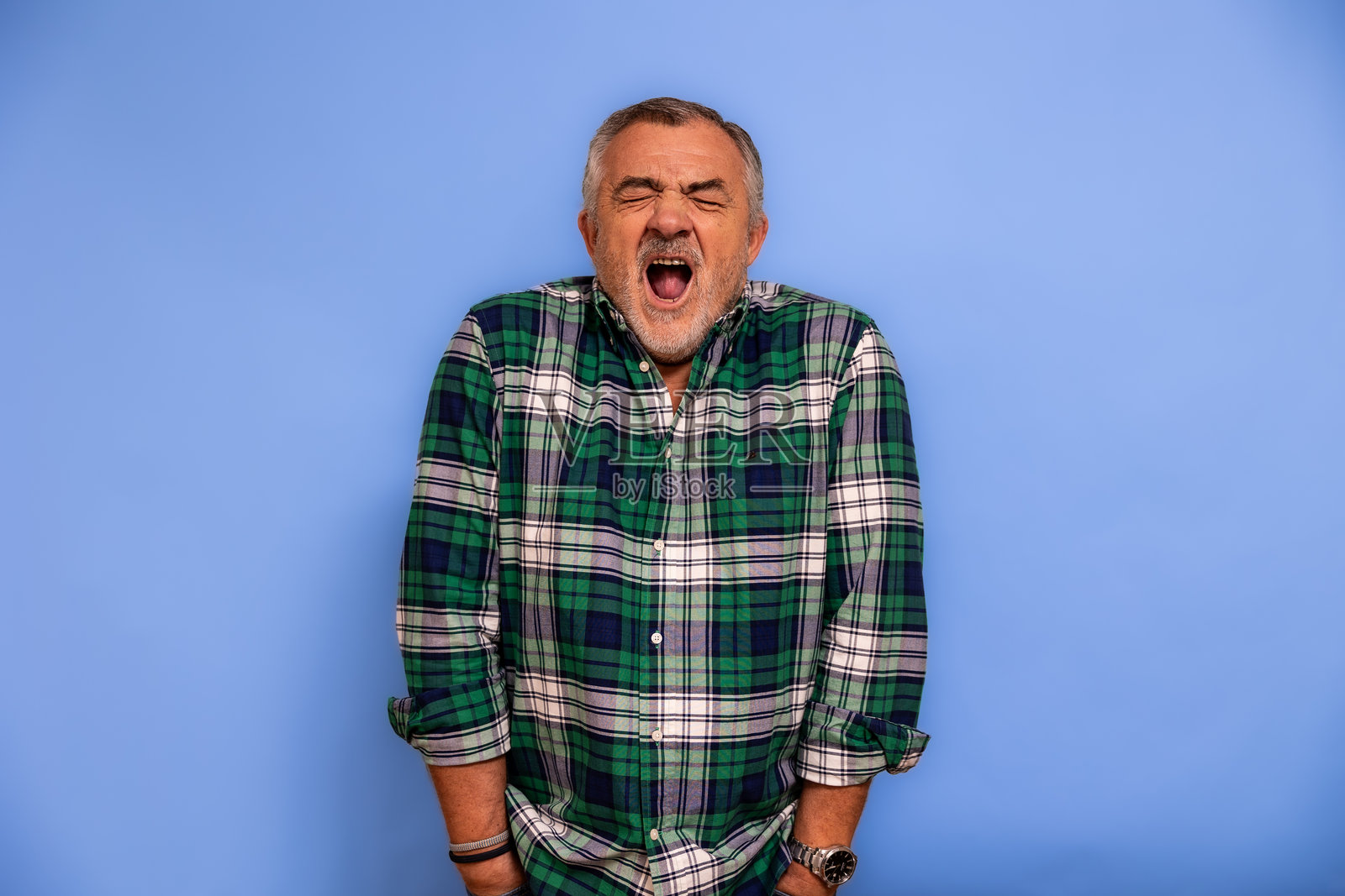 疲惫的老年男子在蓝色背景下打哈欠，感到困倦照片摄影图片