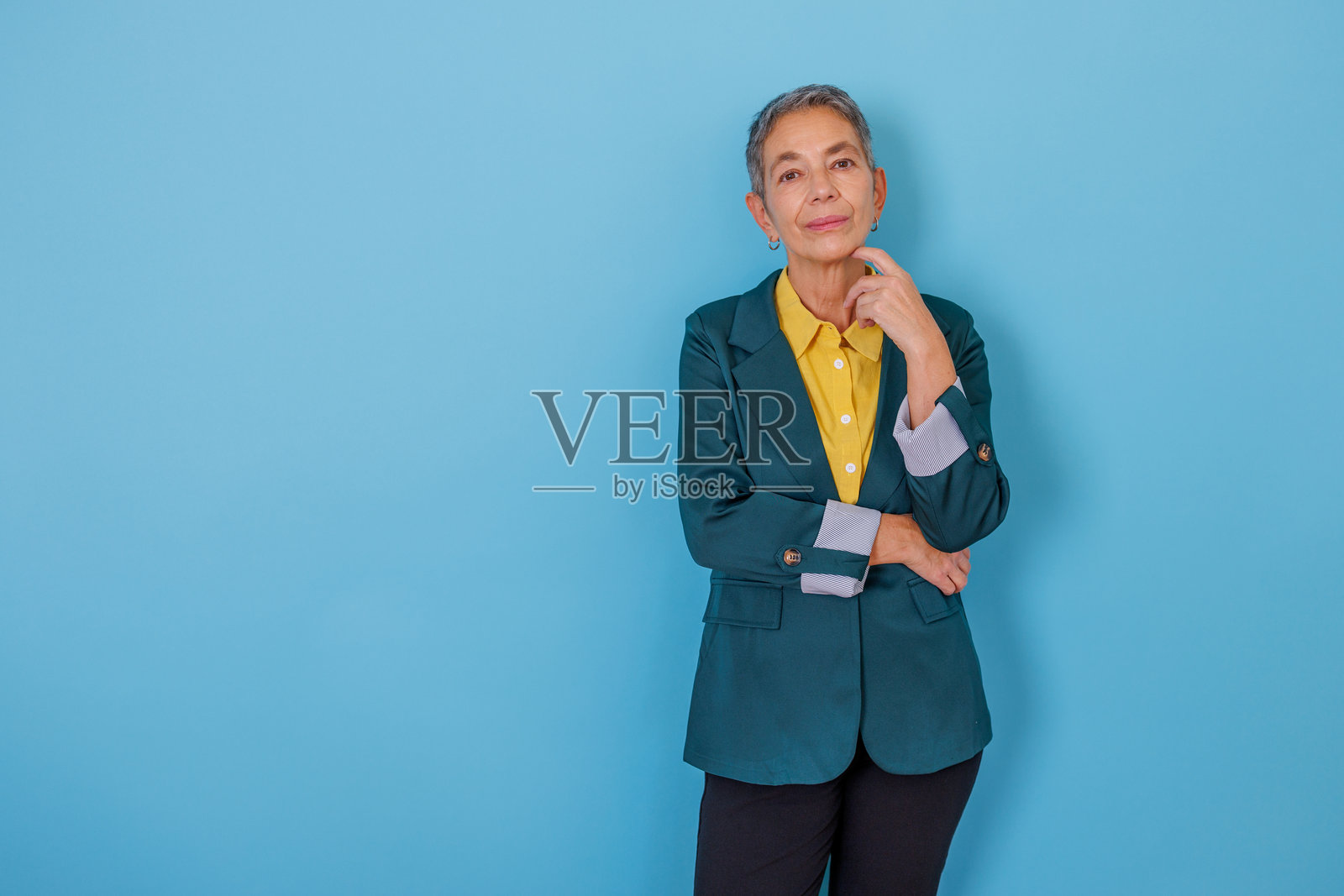 一位成熟的女商人在蓝色背景前自信地摆姿势，她留着短灰发，直视镜头，若有所思。照片摄影图片