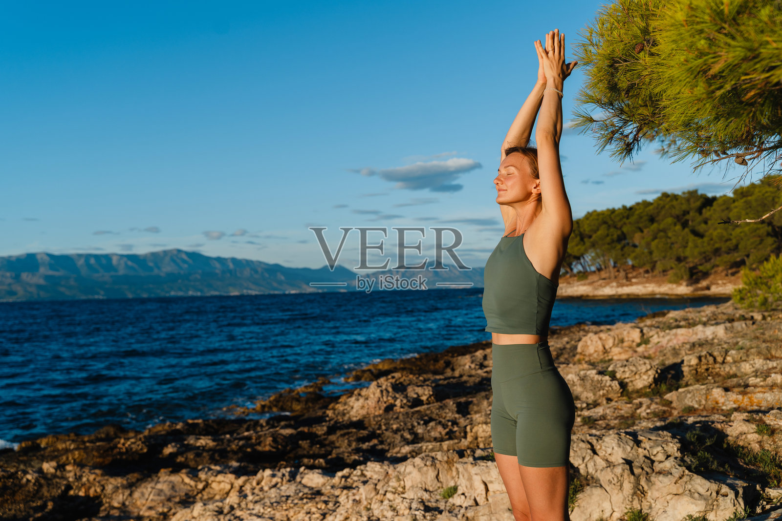 在美丽自然风光的海边，一位优雅的女性正在练习瑜伽。这位女性在海滩的松树林中锻炼，练习着力量和伸展的瑜伽体式。照片摄影图片