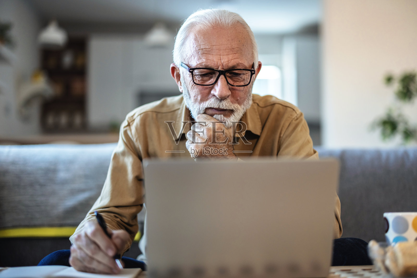 老年人，在文件、表格或退休/人寿保险单上书写，手部特写。养老金领取者在家中，使用笔记本电脑填写法律协议或笔记，并签名。照片摄影图片