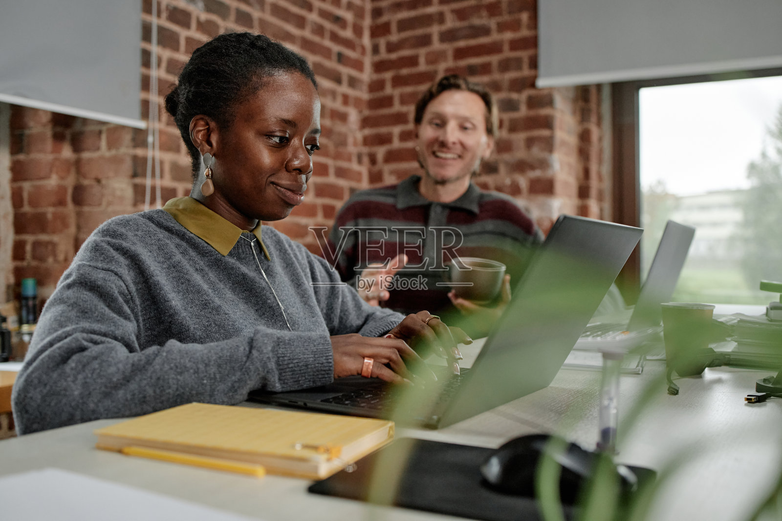 年轻的黑人女性在笔记本电脑上工作，中年白人男性在交谈照片摄影图片