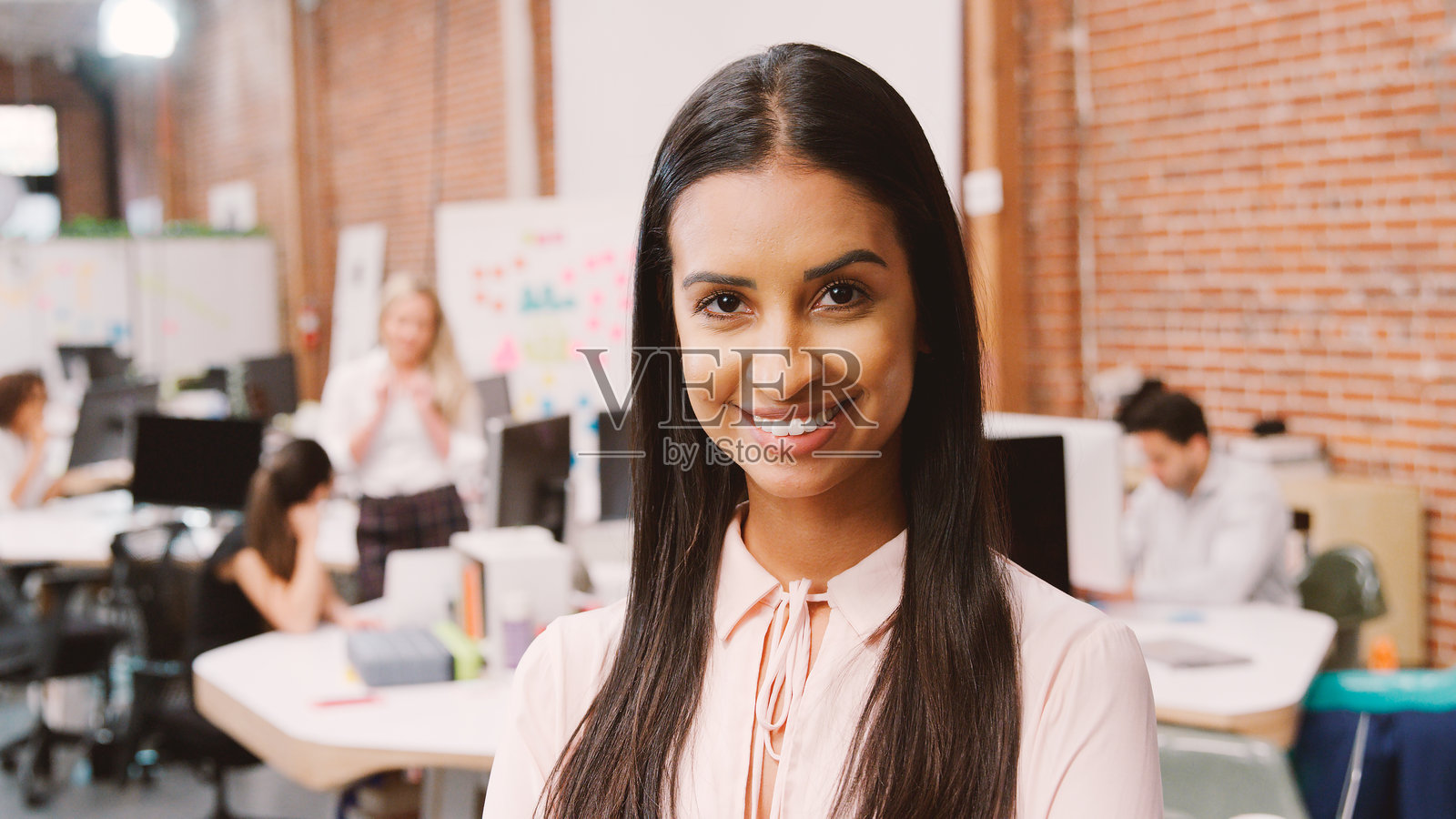 现代办公室里，一位面带微笑的年轻女商人在砖墙前摆出肖像照照片摄影图片