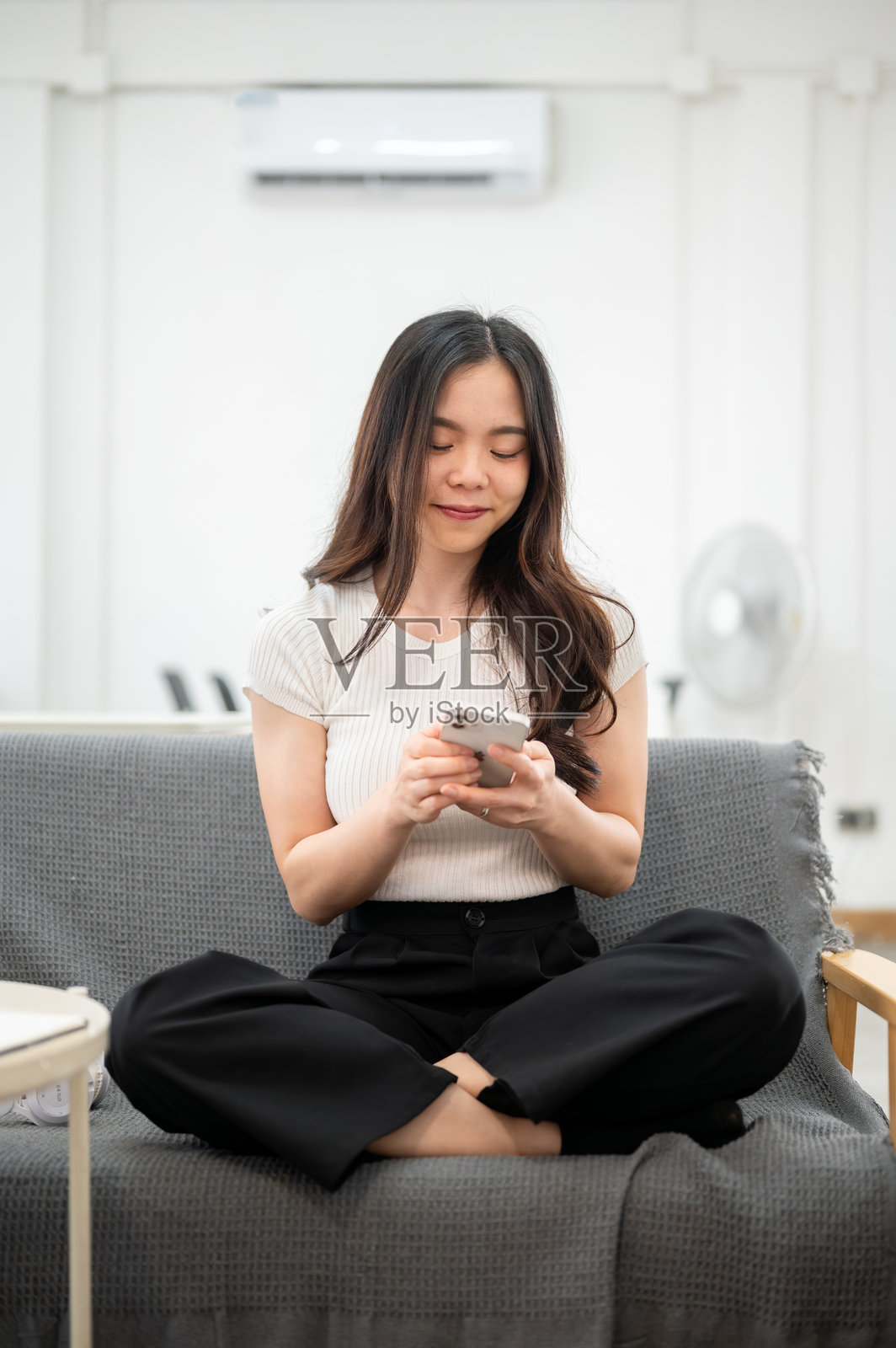 亚洲女性坐在沙发上，双腿叠放，双手持手机观看照片摄影图片