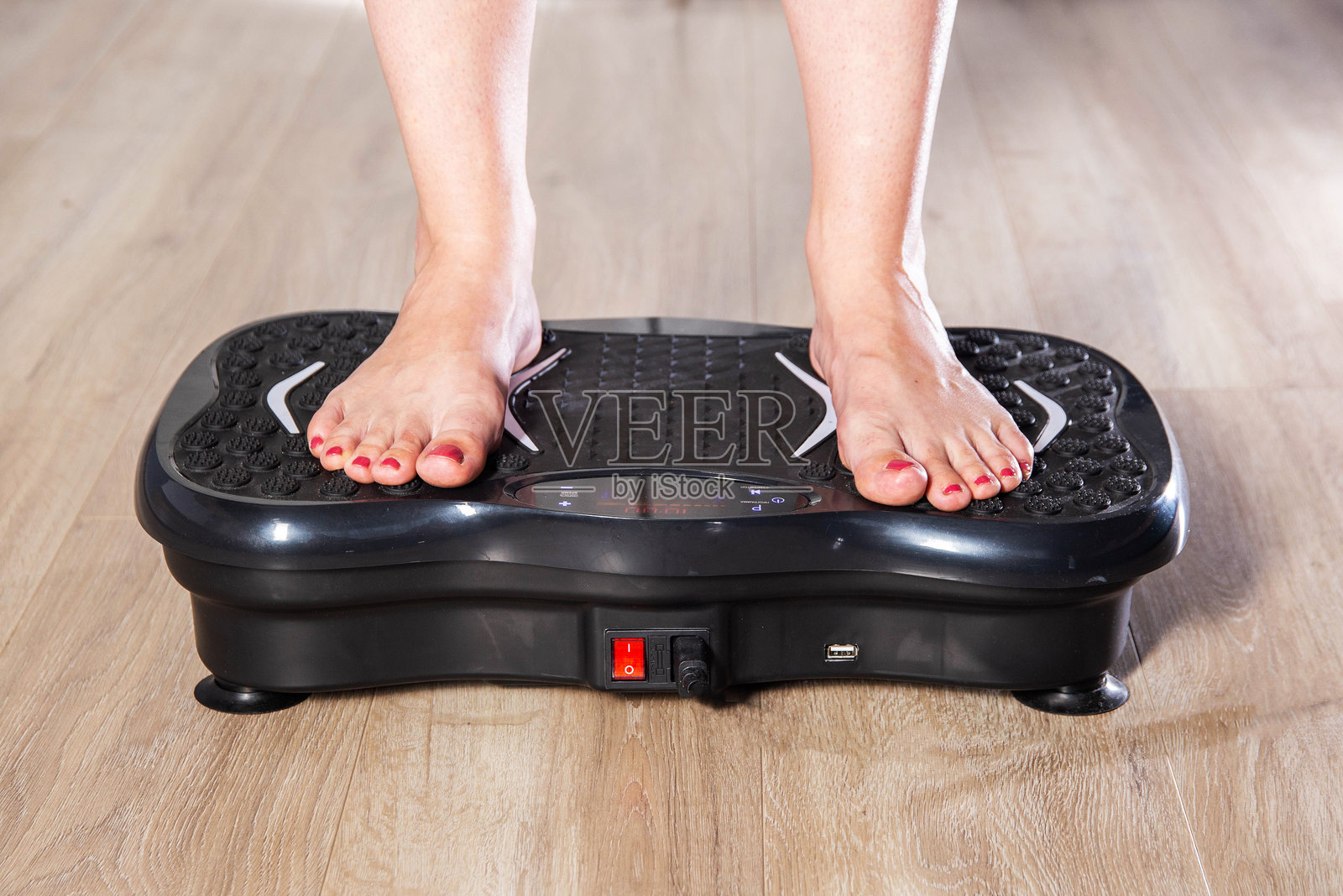 女性的腿站立在家中的健身振动器上。在家做运动的概念。现代家用健身器材，特写。照片摄影图片