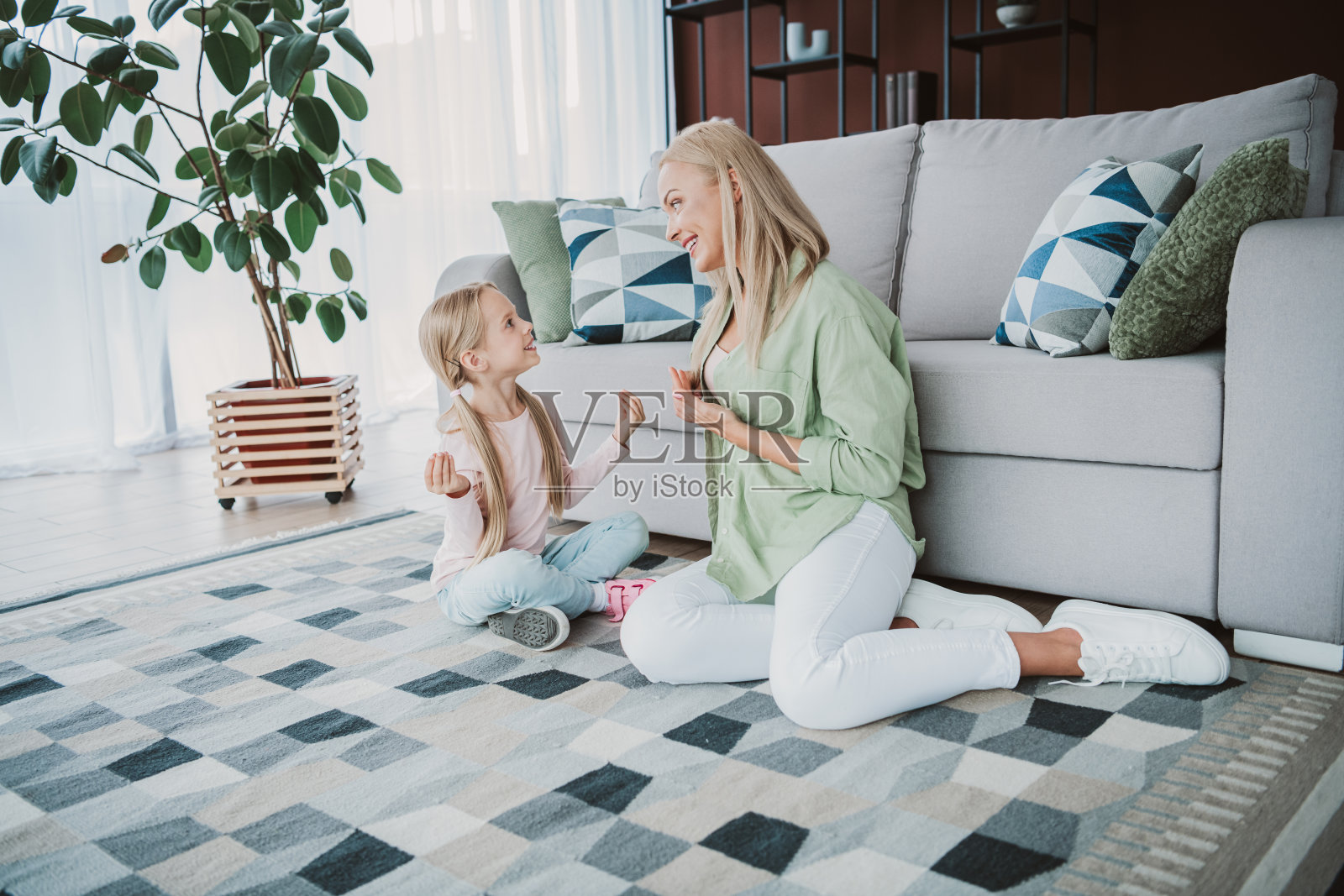 顽皮的母女俩在家里的沙发上享受着舒适的一天，周围有靠垫、地毯和植物，营造出温馨的家庭氛围。照片摄影图片