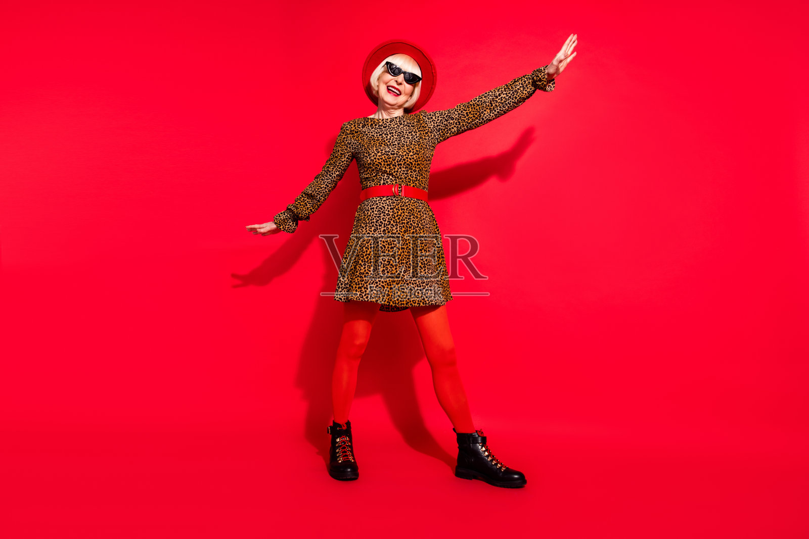 快乐、开朗、友善的老妇人全身照，双手像飞机翅膀一样张开，孤立在红色背景上照片摄影图片