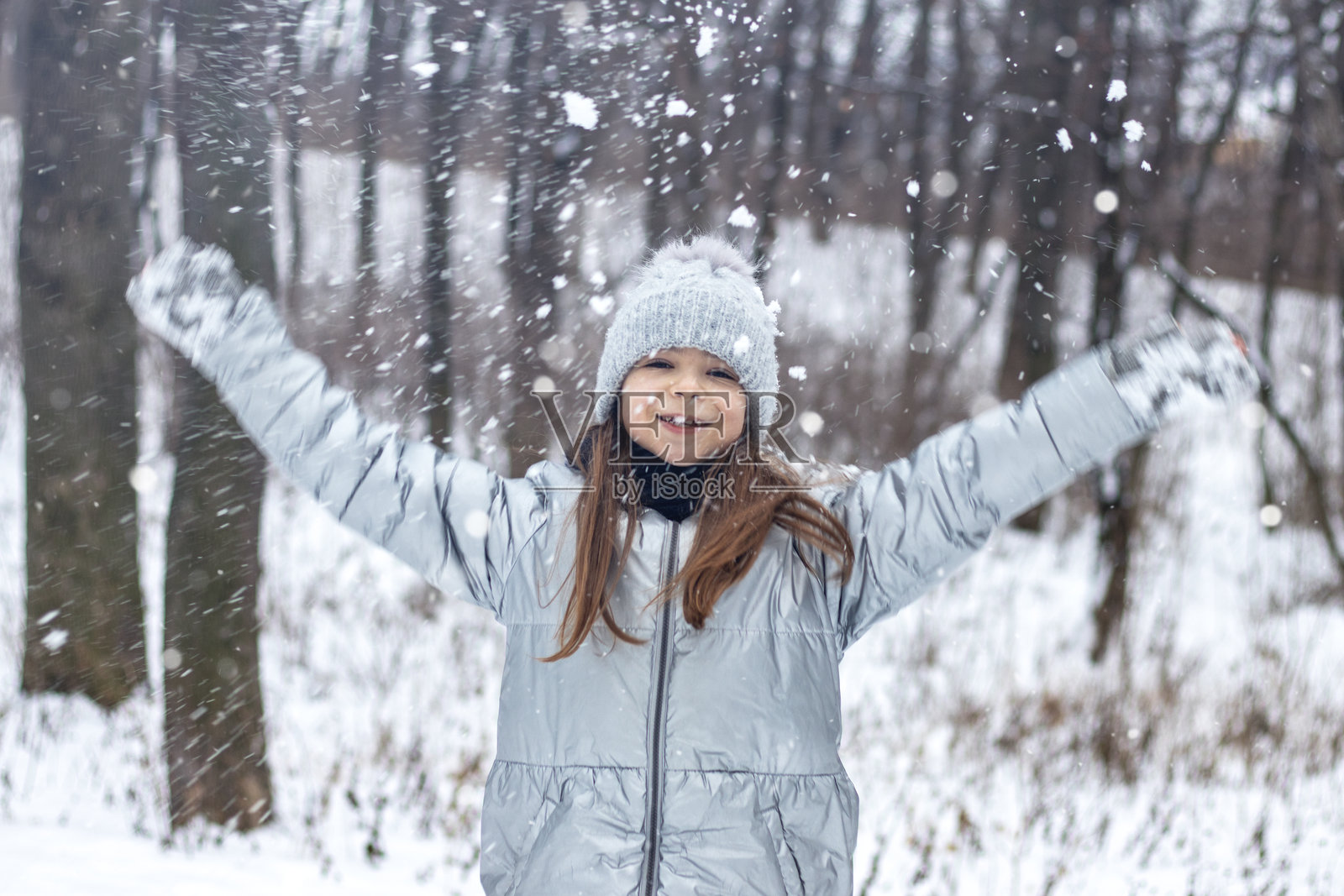 穿着冬装和绒帽的年轻女孩在雪林中举起双臂，欣喜地享受着这一刻照片摄影图片