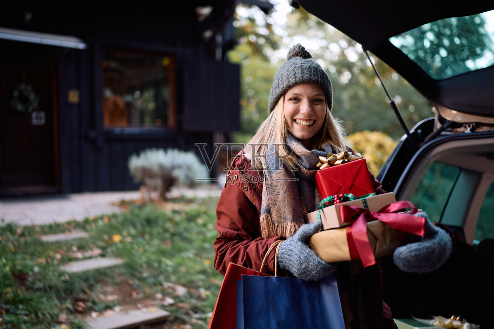 快乐的女士从汽车后备箱取出礼物并看向镜头。照片摄影图片