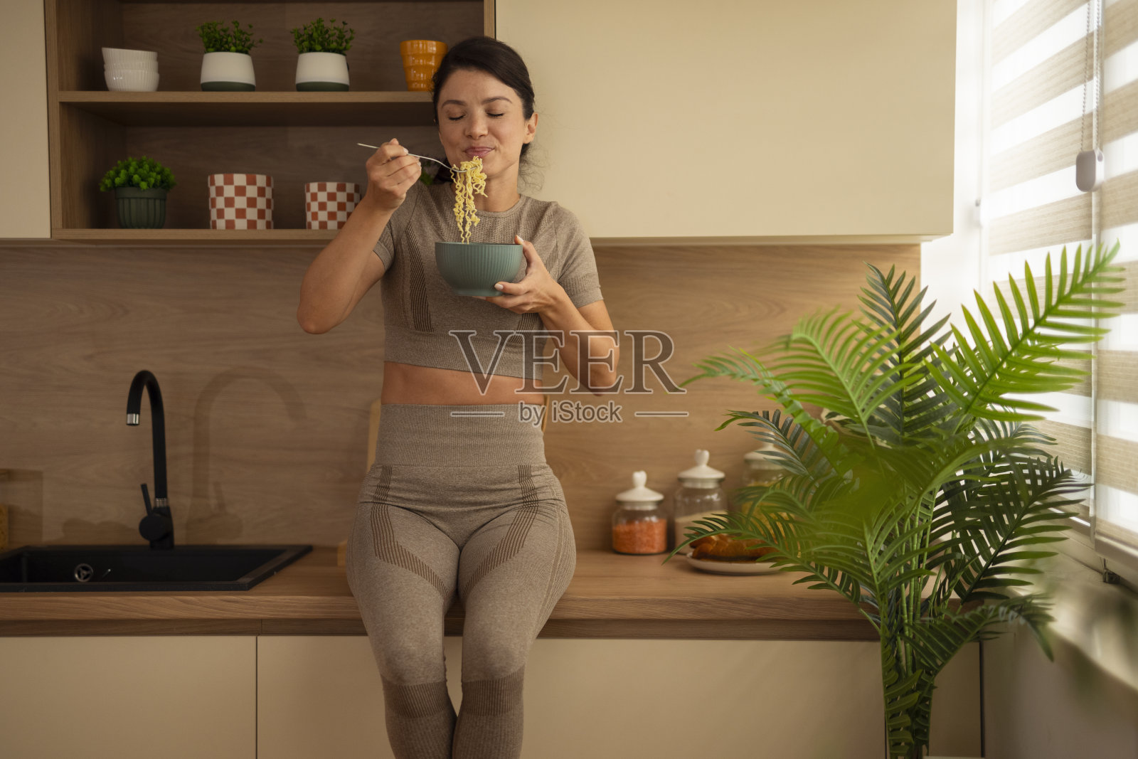 穿着运动服的女性在厨房吃健康面条照片摄影图片