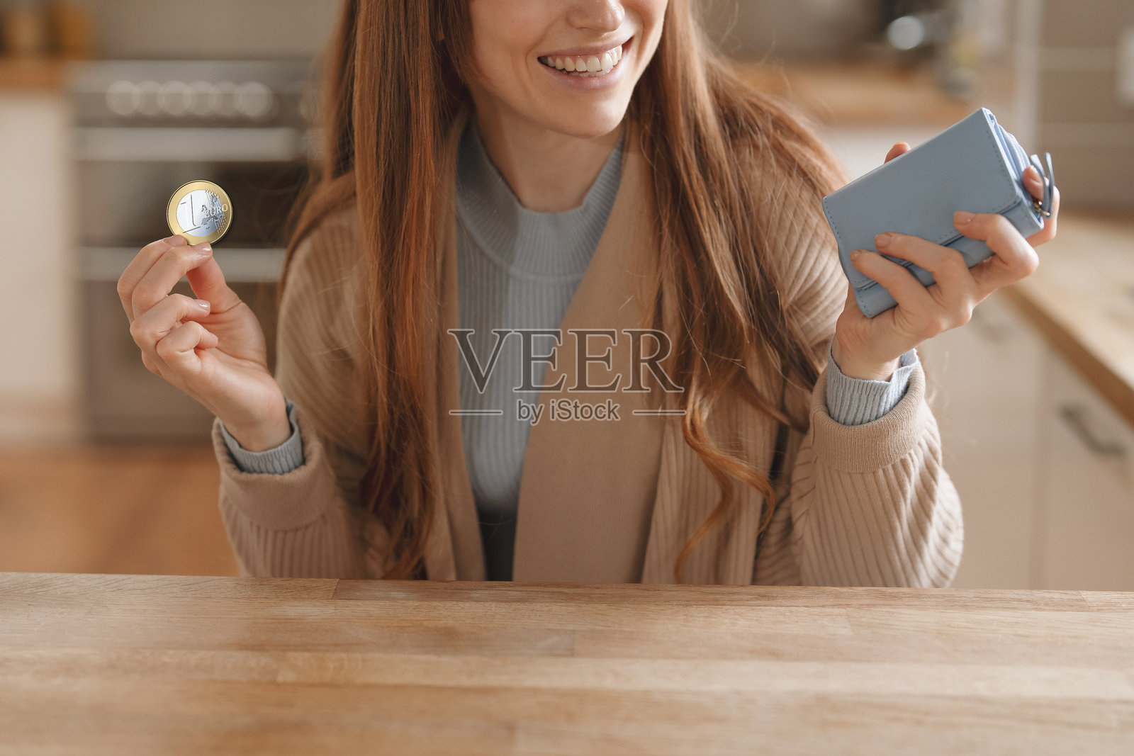 一位女士在明亮的厨房里，手里拿着一枚硬币和一个小钱包照片摄影图片