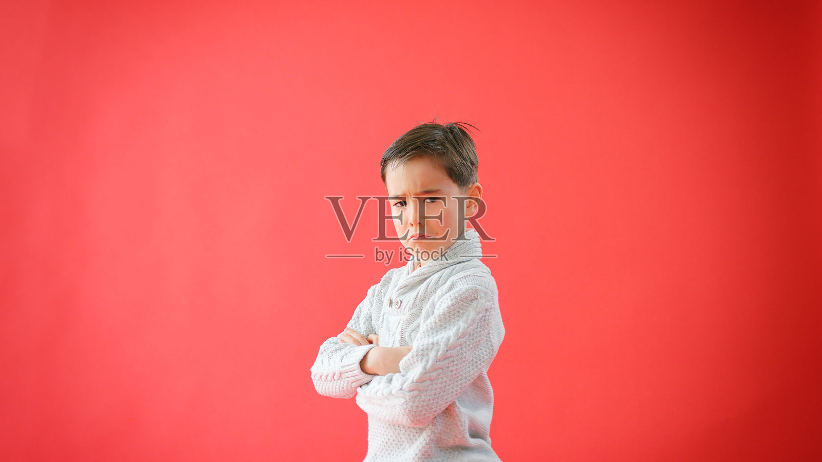 身穿红色背景的严谨的年轻男孩，双臂交叉，面带严肃的肖像照照片摄影图片