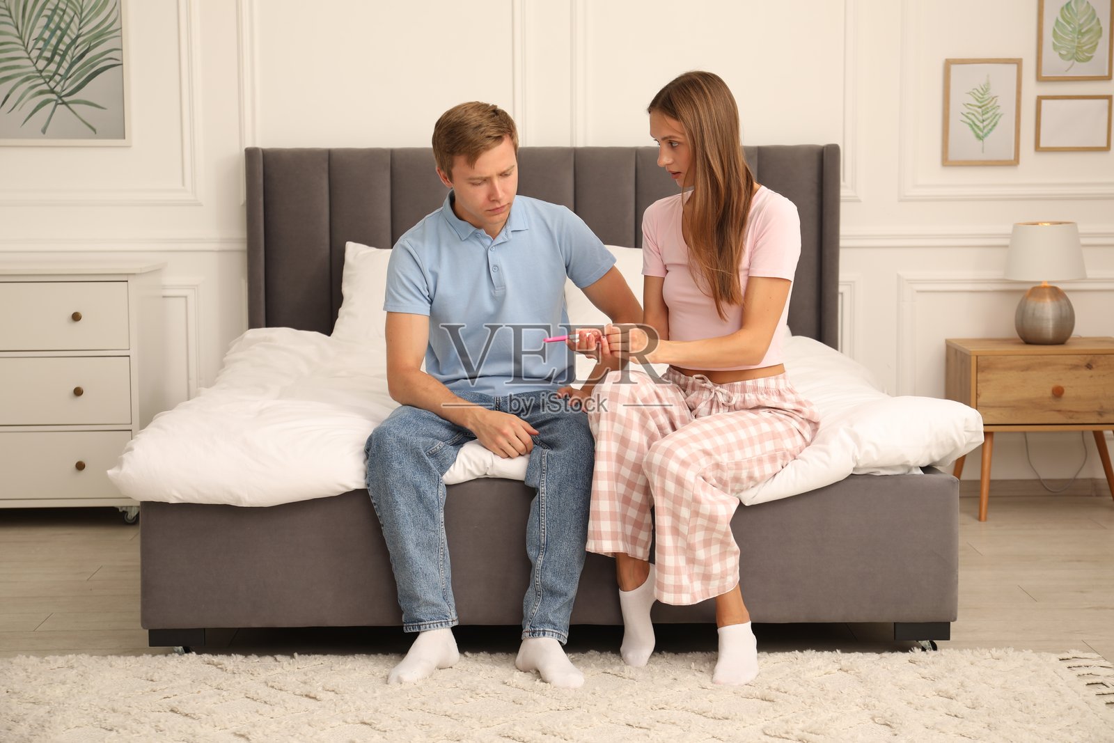 一对在家中床上，手持验孕棒、面露担忧的夫妇照片摄影图片