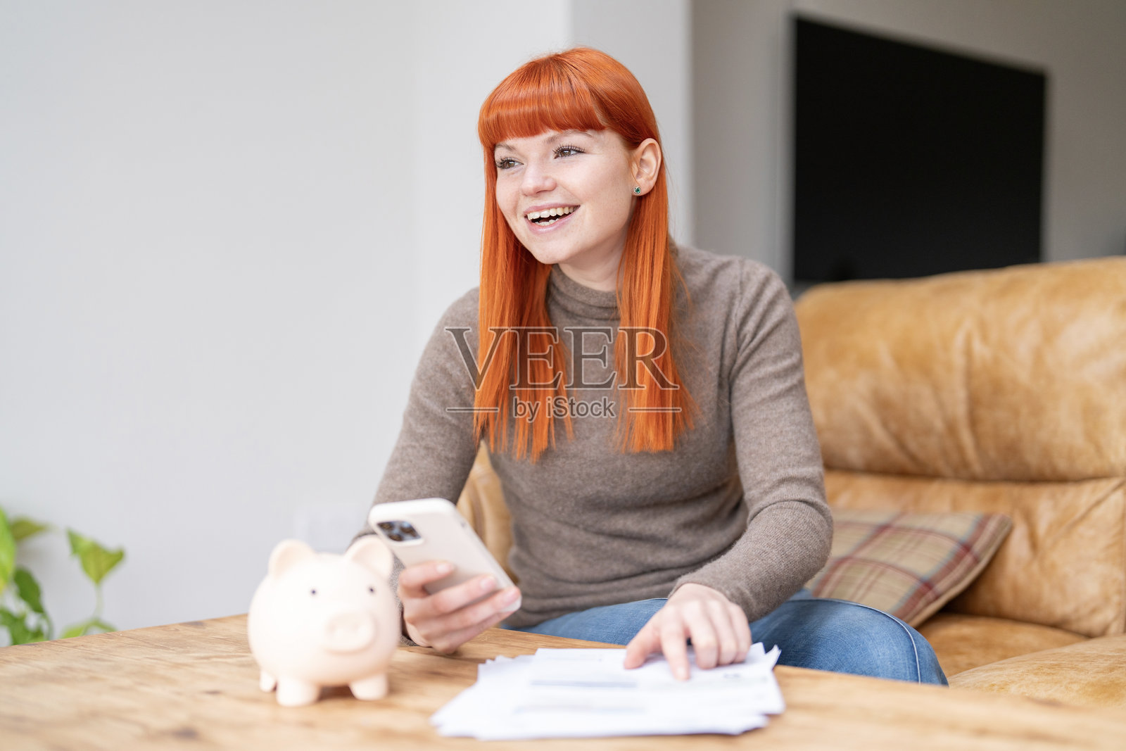 年轻女子用手机和存钱罐查看财务状况照片摄影图片