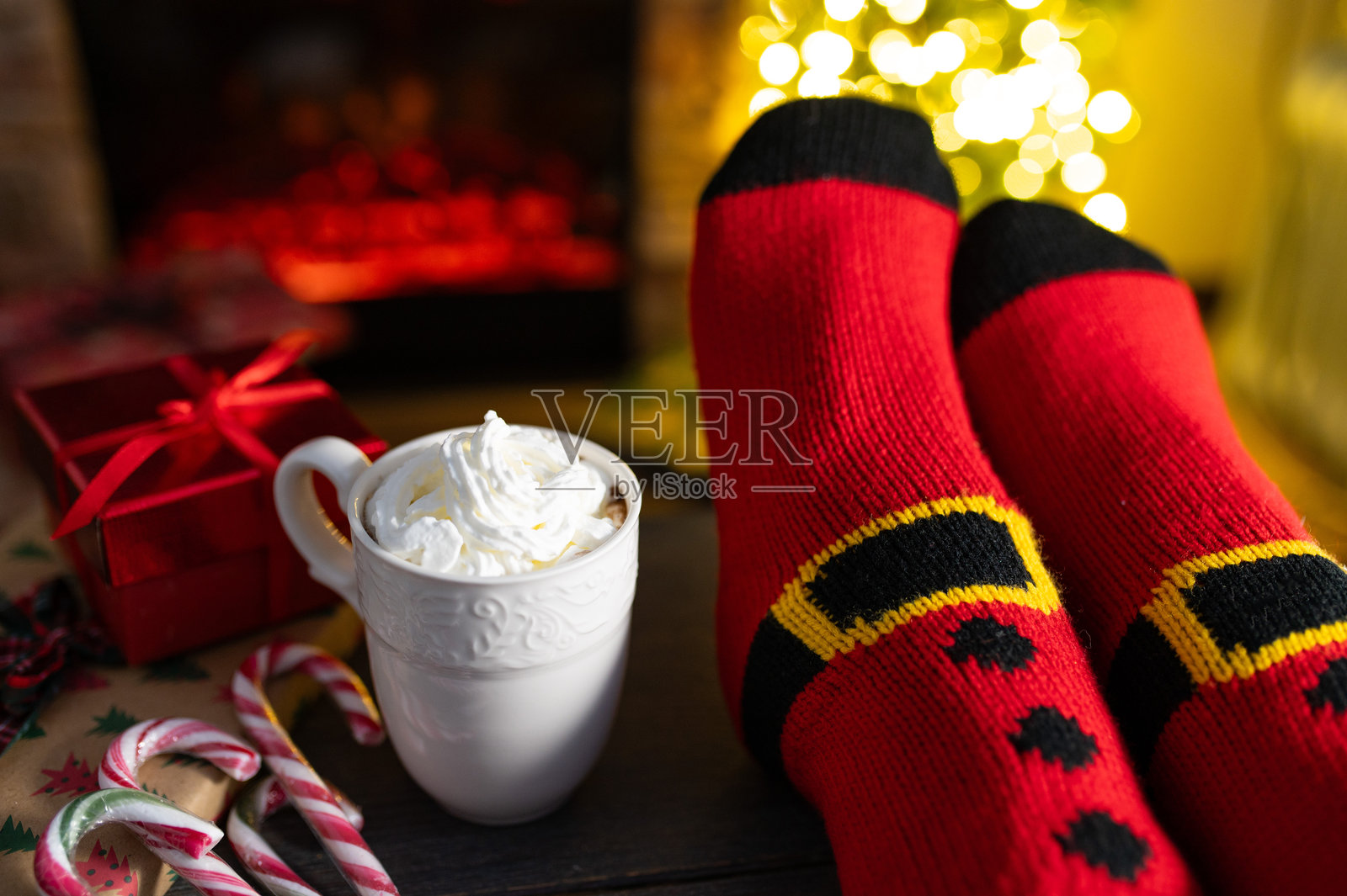 穿着圣诞袜子的女性腿部，背景是带壁炉的室内和深色墙壁。留有您的装饰空间。照片摄影图片