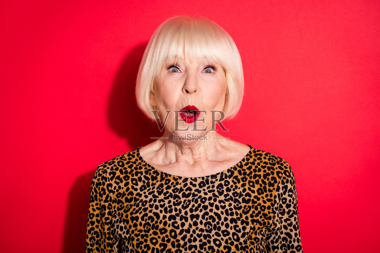 一名惊讶、震惊、惊叹、印象深刻的老妇人对促销活动的反应，孤立在红色背景上照片摄影图片