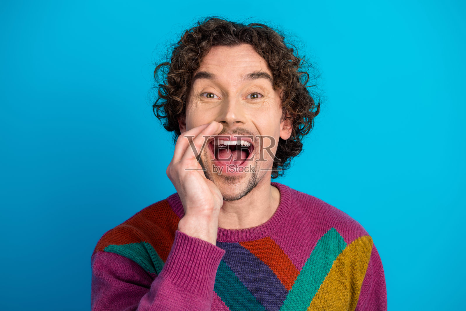 身穿彩色毛衣的年轻英俊男子，卷发，在蓝色背景前微笑照片摄影图片