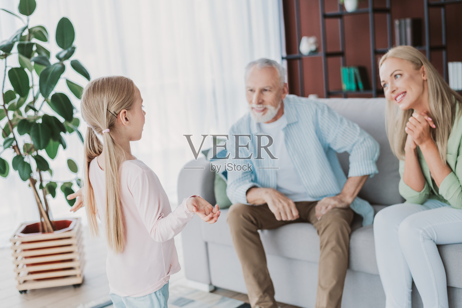 一个快乐的女孩和她的祖父母在家中聊天，温馨的家庭在有植物、书架和大窗户的舒适客厅里增进感情照片摄影图片