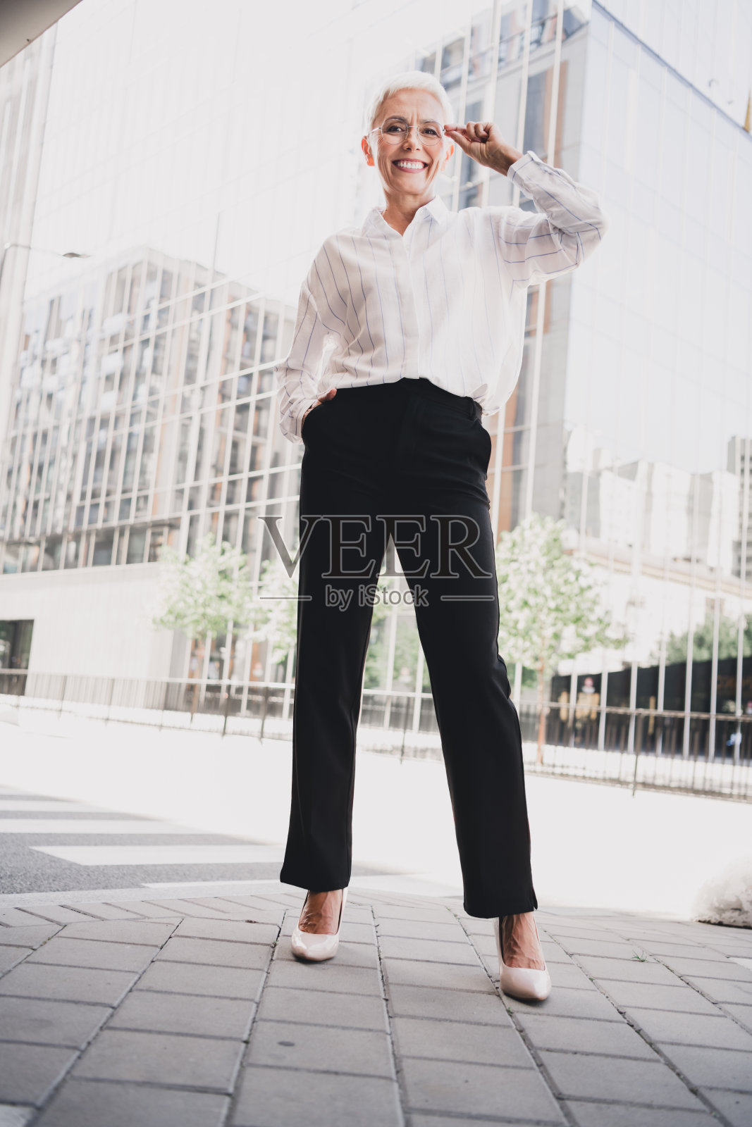 一位自信的年长女商人在现代城市景观中摆姿势，身着正装和时尚高跟鞋，适合都市领导力和时尚主题。照片摄影图片