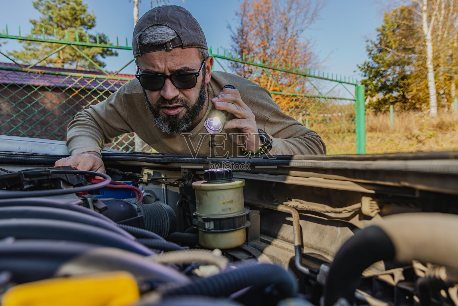 下午阳光下，一名男子正用手电筒检查汽车发动机照片摄影图片