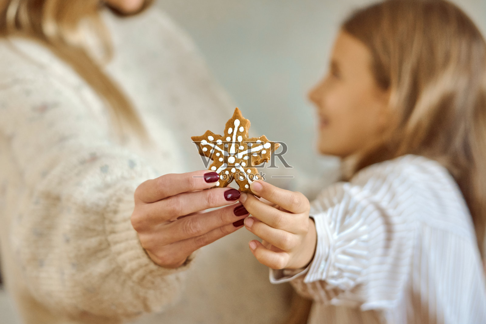 温馨的节日厨房里，母女俩分享着一块缀有糖霜的星形饼干照片摄影图片