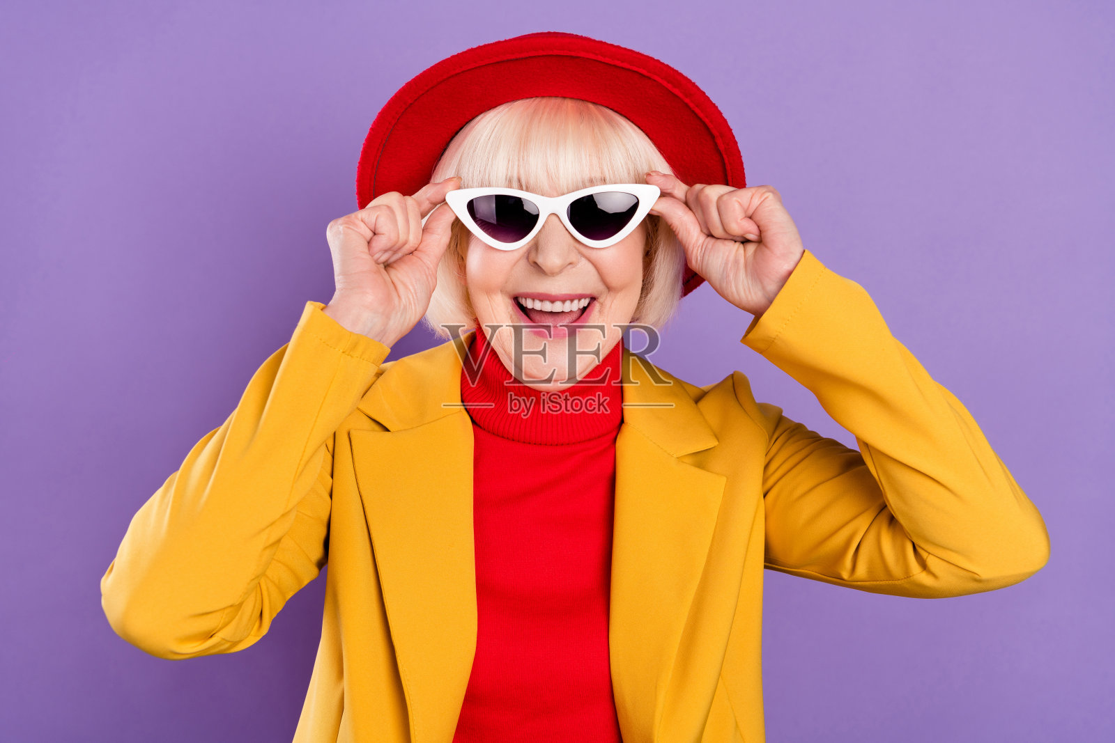 身穿黄色夹克和帽子、戴着眼镜的滑稽短发老妇人肖像，孤立在紫色背景上照片摄影图片