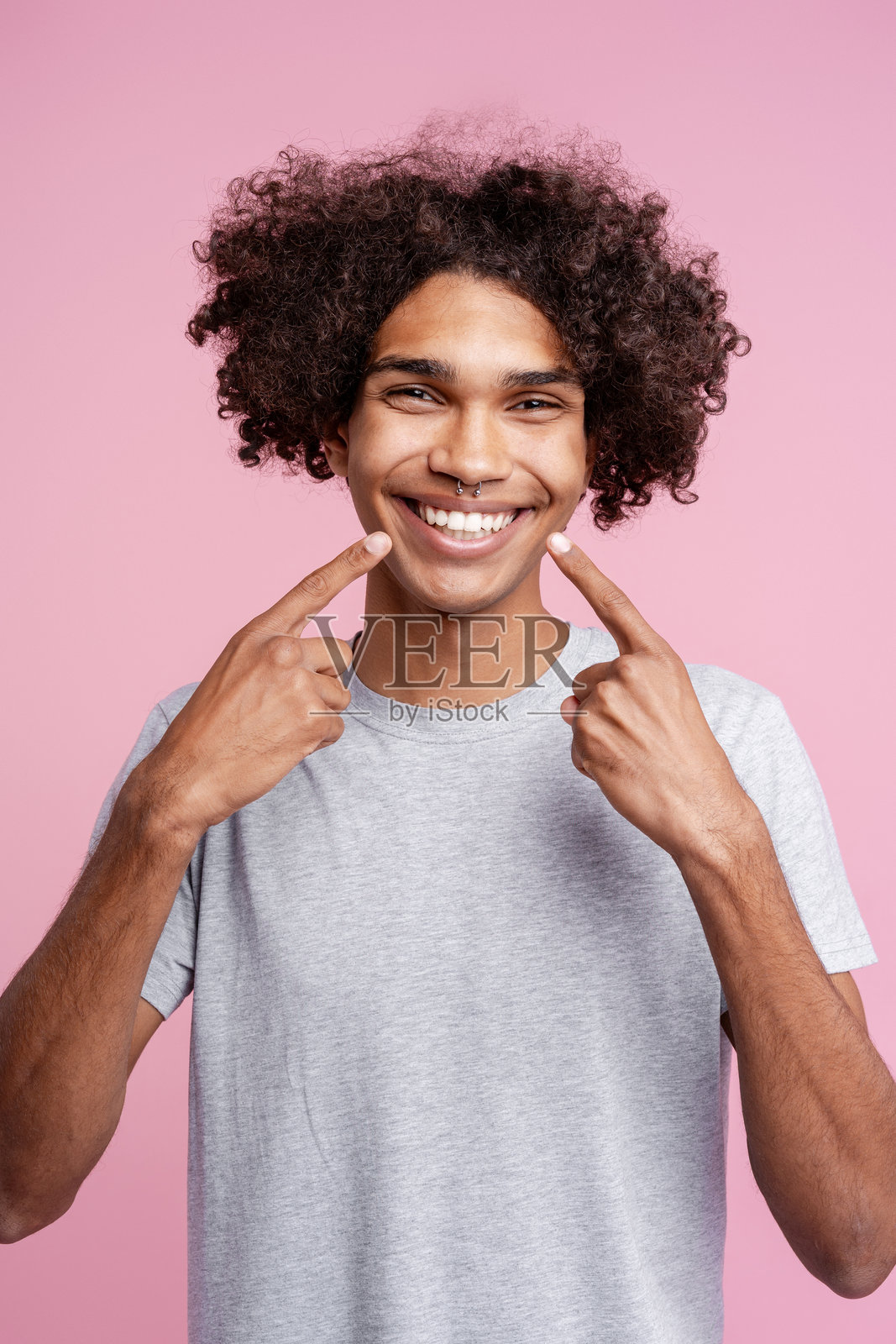 英俊的年轻非裔美国男子，手指点着牙齿，面带微笑，孤立在粉色背景上照片摄影图片